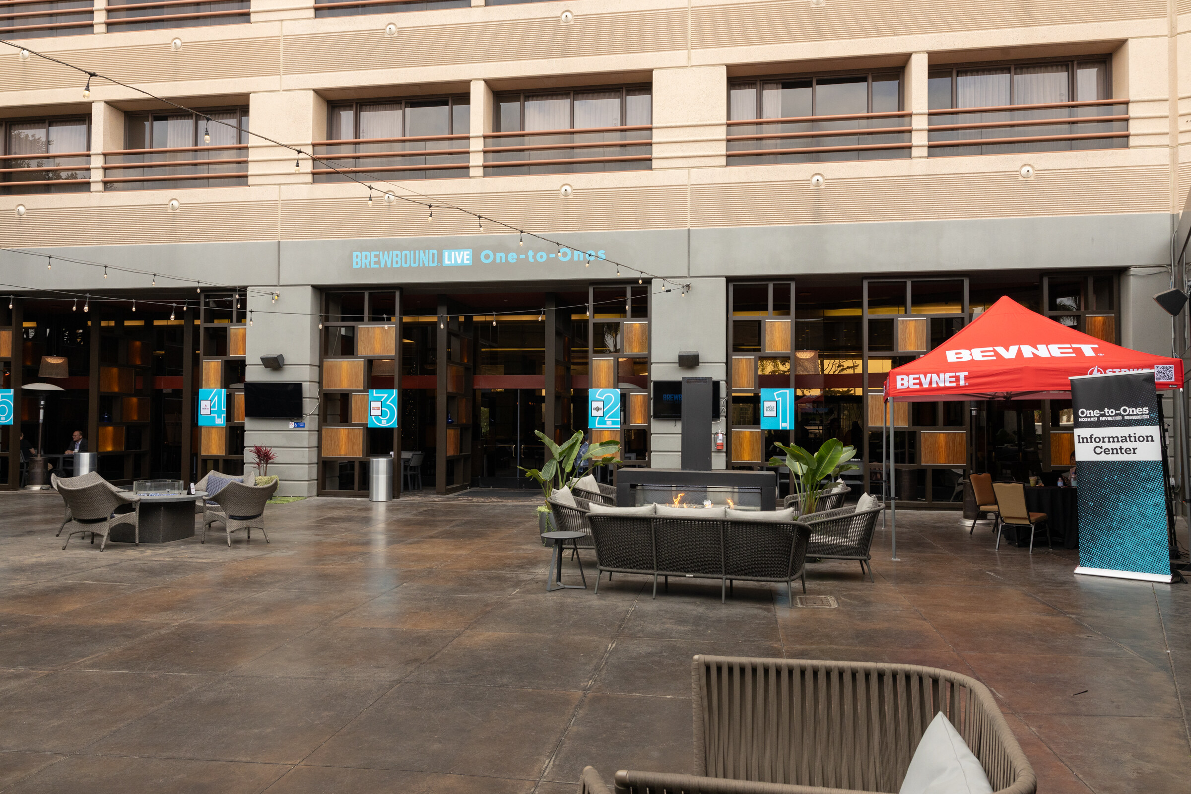 A courtyard with tables and a red BevNET tent beneath a Brewbound Live One-to-Ones sign.
