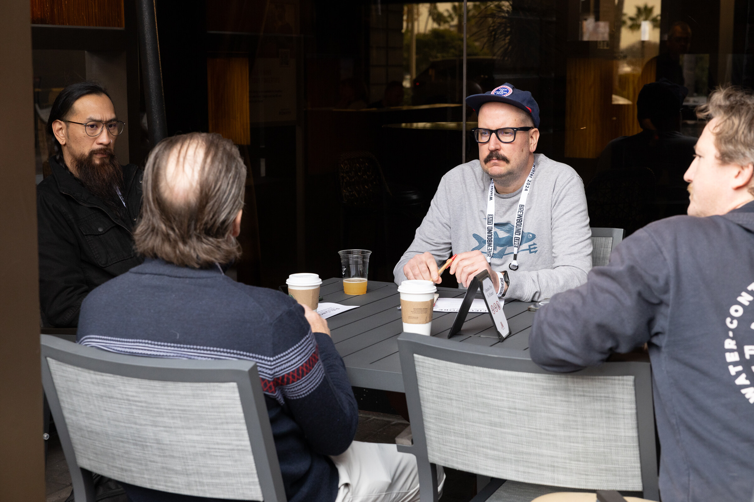 Four men sit around a small table with coffee cups.