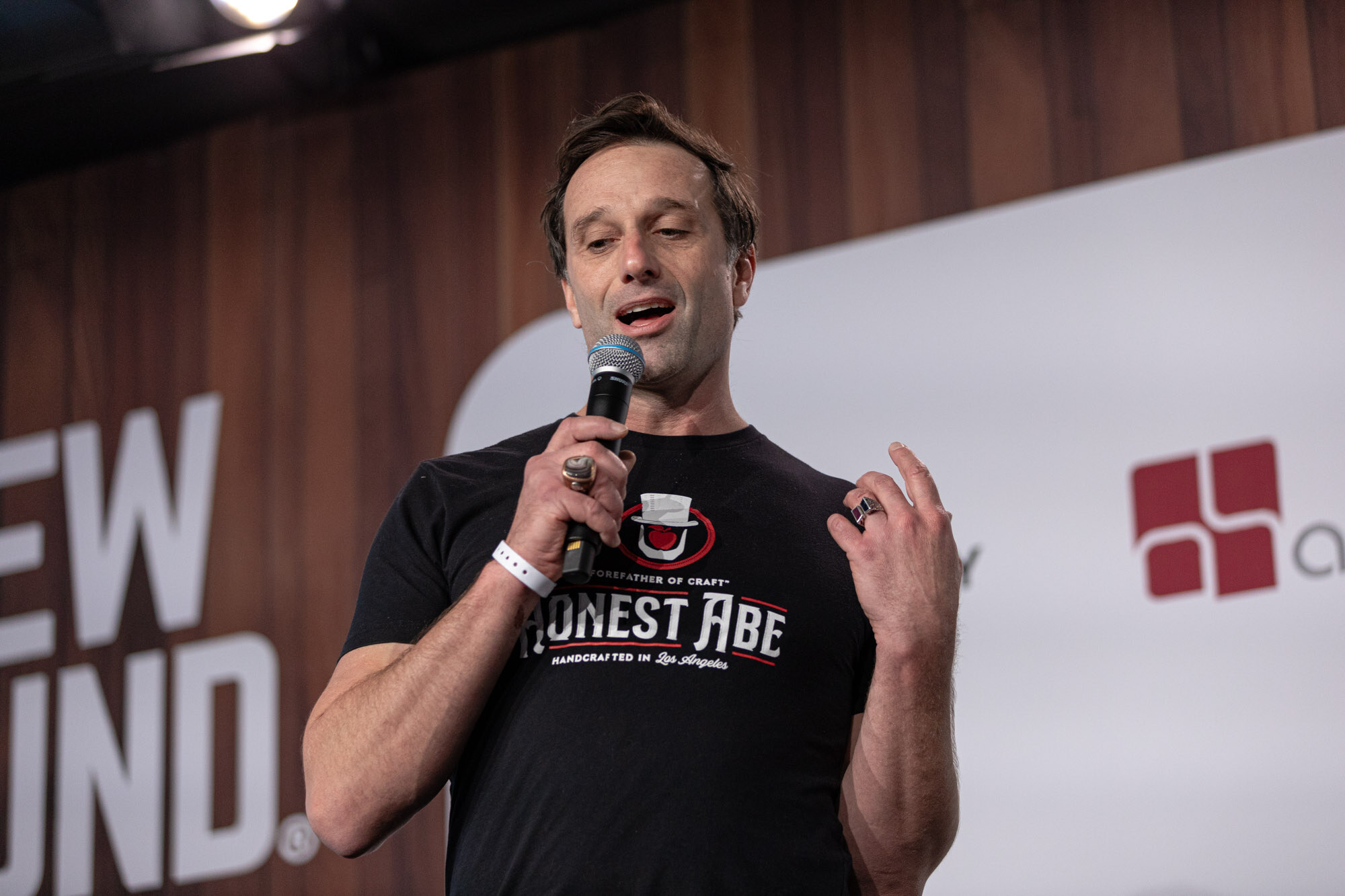 A man in a black Honest Abe t-shirt speaks into a microphone against a Brewbound Live backdrop.