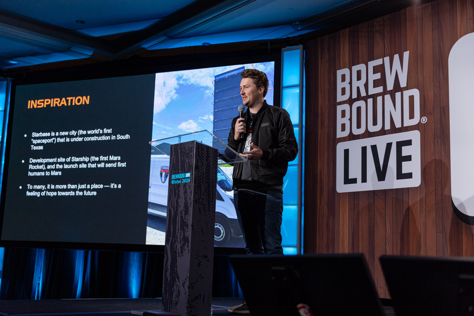 A man in a dark jacket stands at a podium next to a slide titled Inspiration about Starbase.