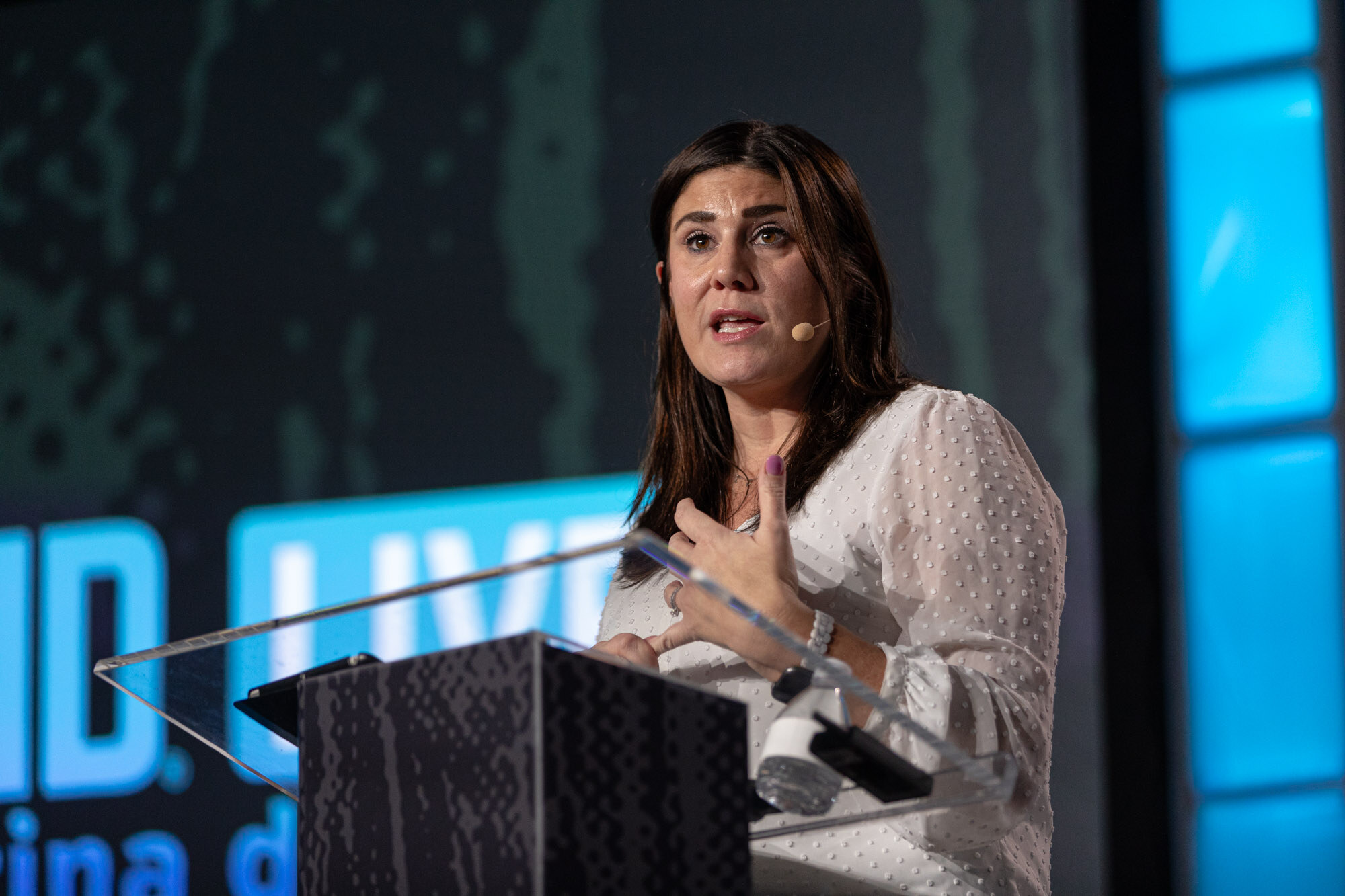 A woman in a white blouse speaks from a podium in front of a Brewbound Live screen.