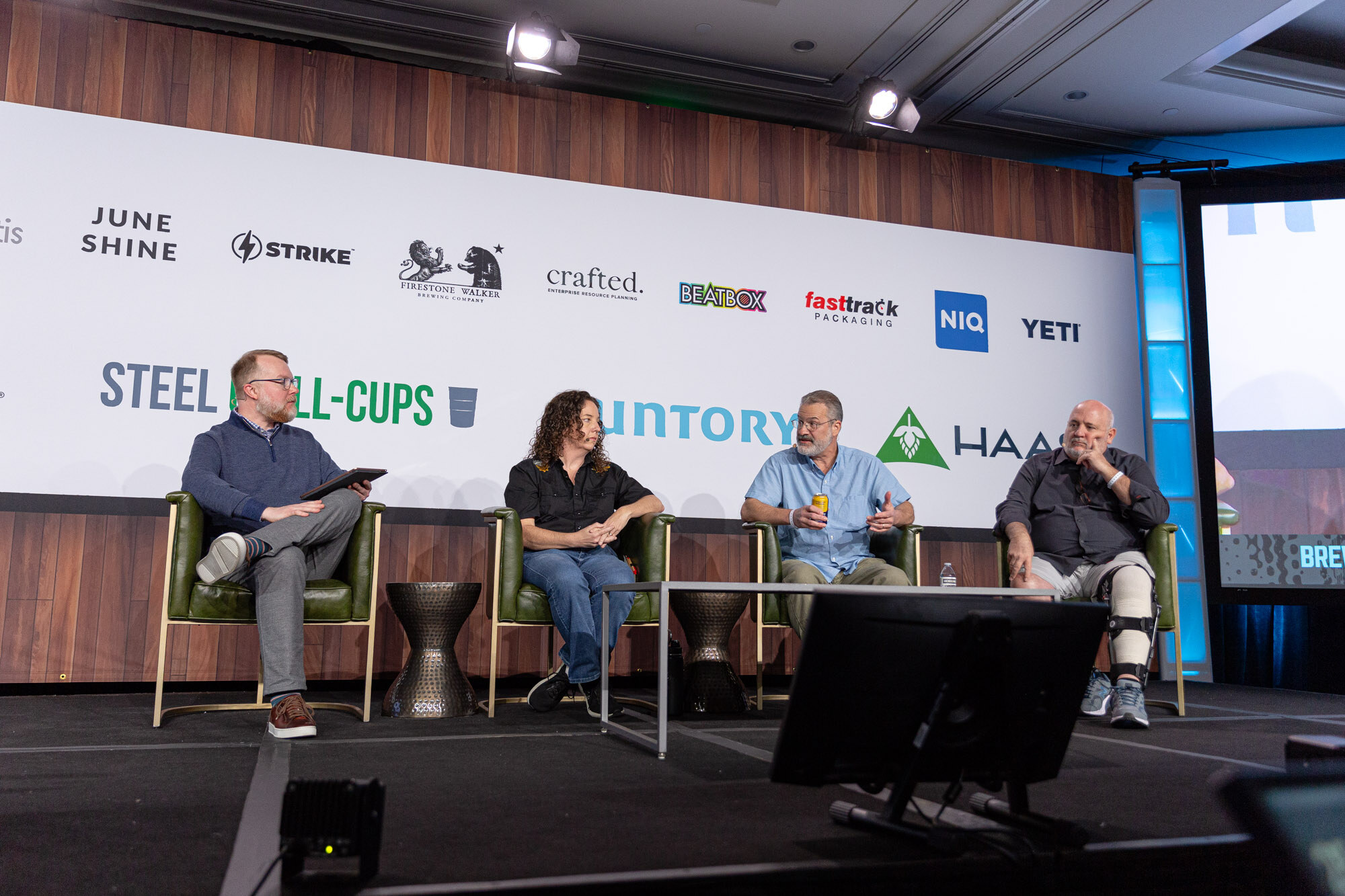 Four people sit in a row on stage in front of the sponsor wall.