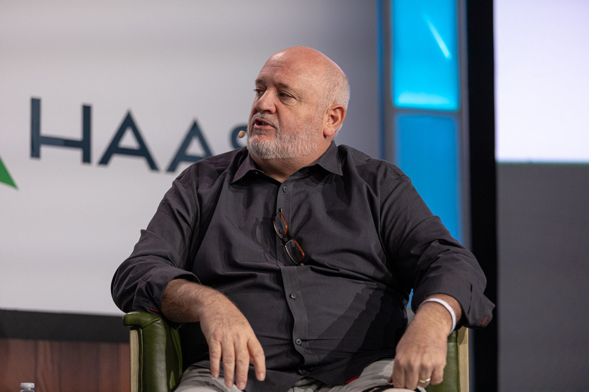 A bearded man in a dark shirt sits in an armchair in front of a Haas sign.