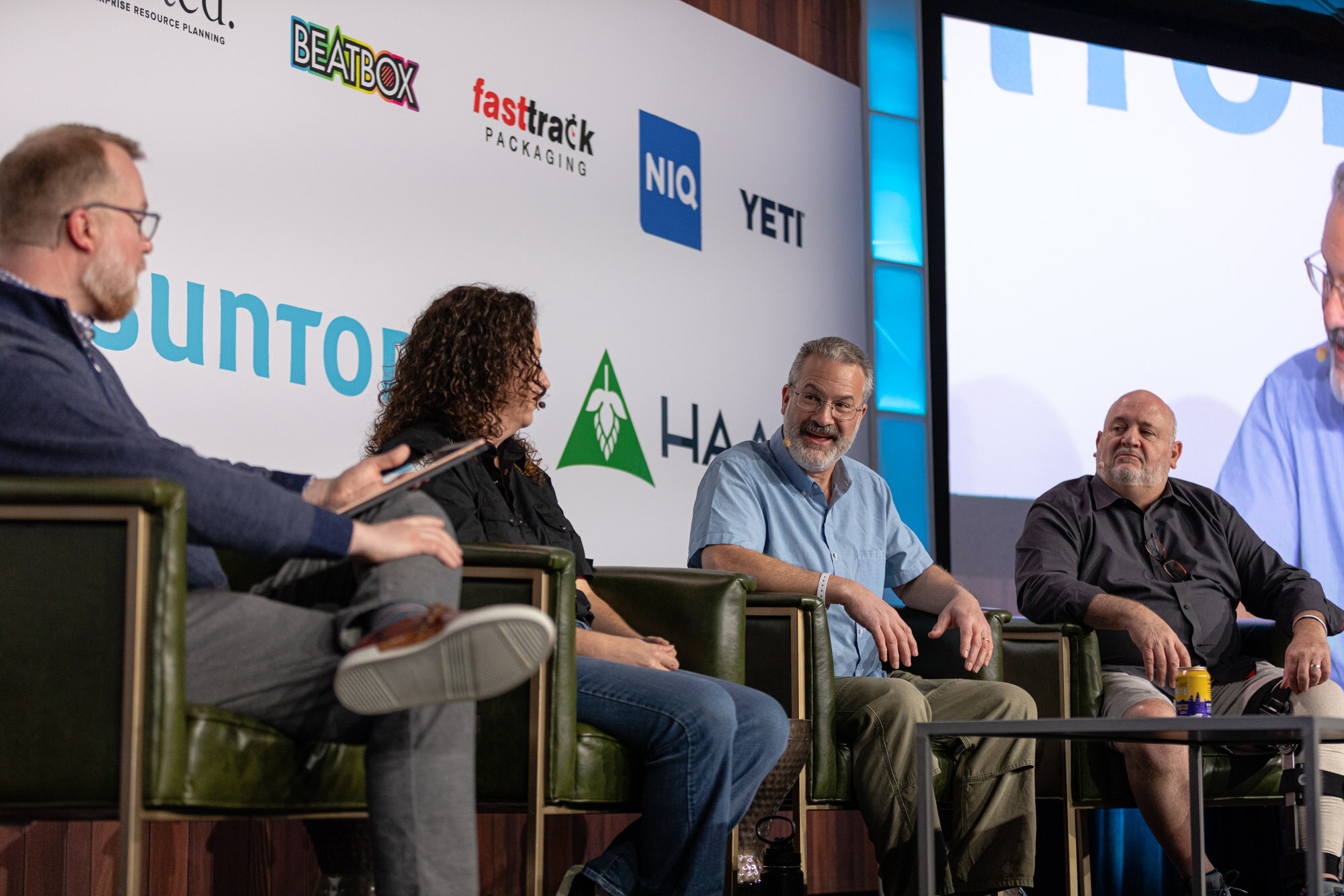 Four people sit in armchairs, with a man on the left holding a tablet.