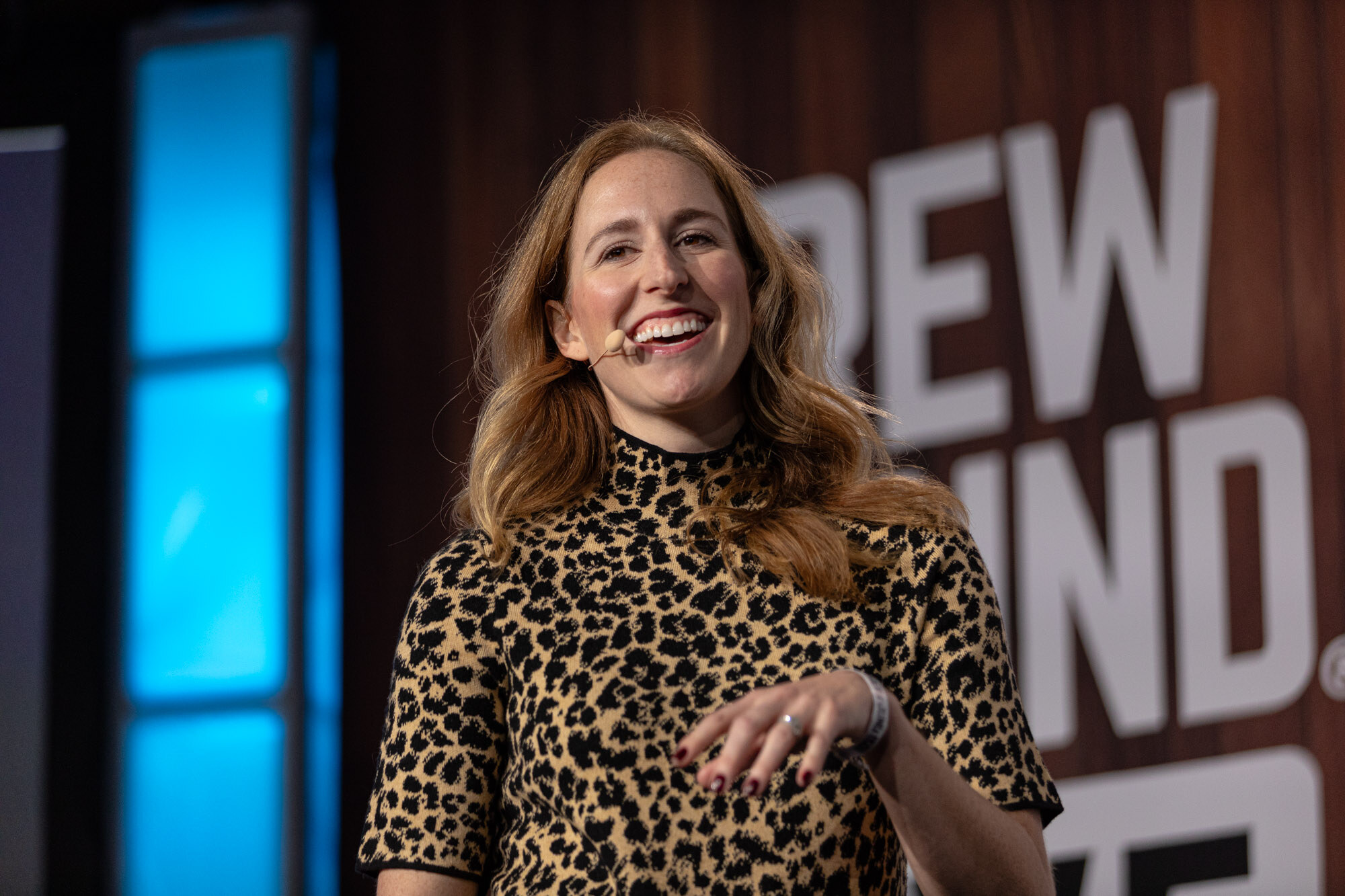 A woman in a leopard-print dress laughs on stage in front of a Brewbound Live sign.