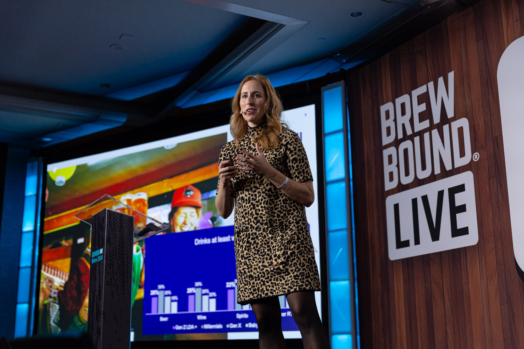 A woman in a leopard-print dress stands beside a screen with a bar chart and photos.