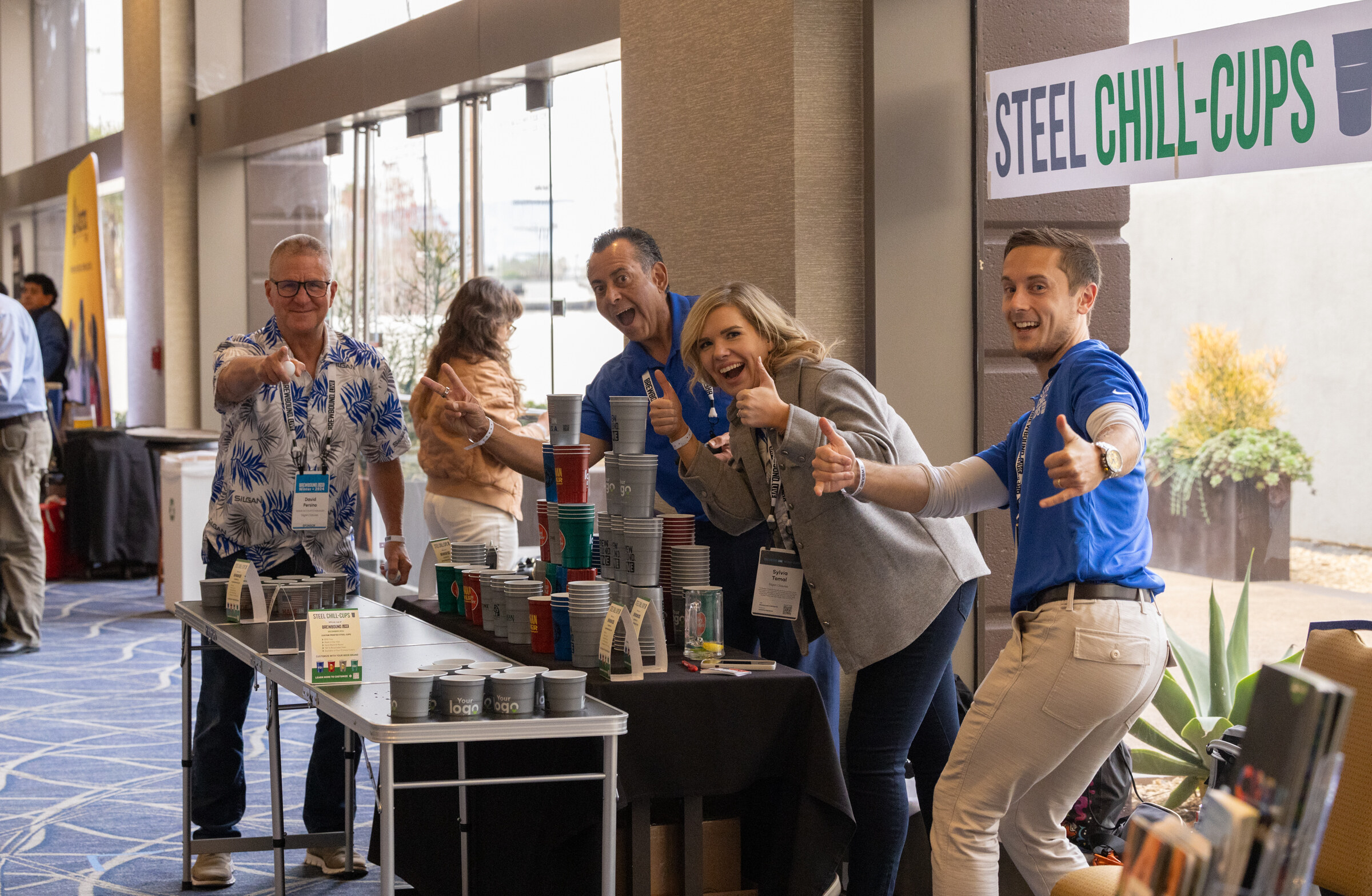 Four people at a table of metal cups give thumbs up to the camera.