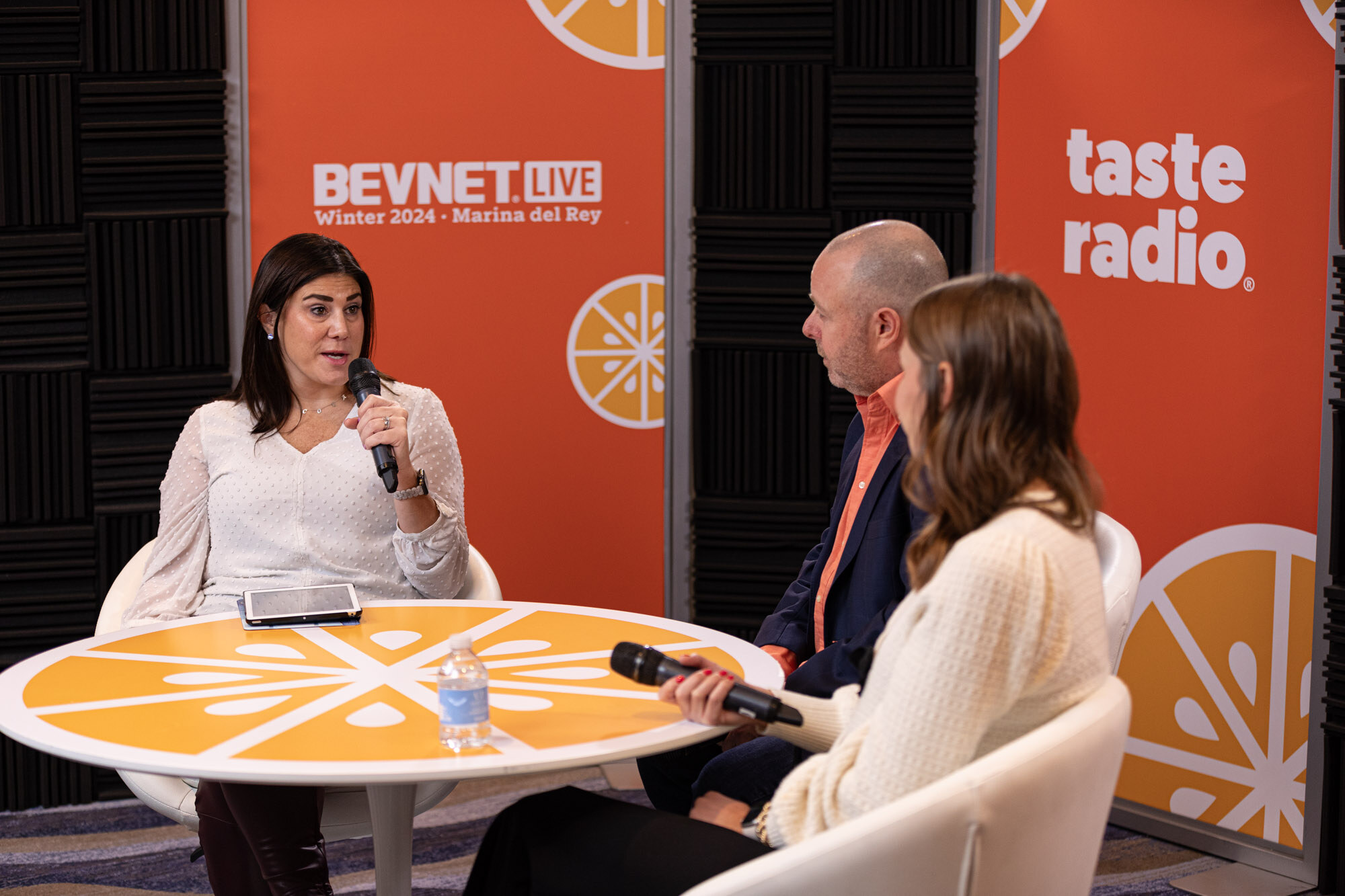 Three people sit around an orange table in front of a banner reading BevNET Live Winter 2024 Marina del Rey.