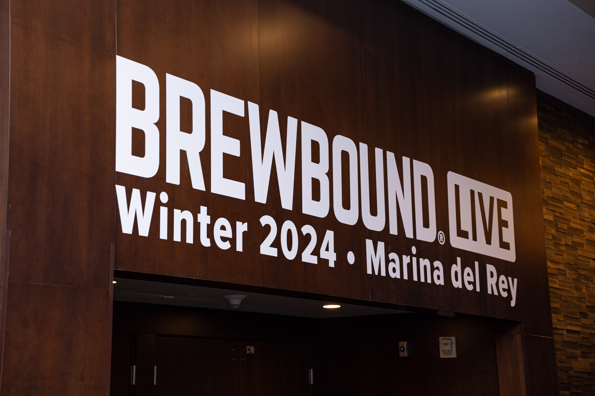 A white Brewbound Live Winter 2024 Marina del Rey sign on a dark wood wall.