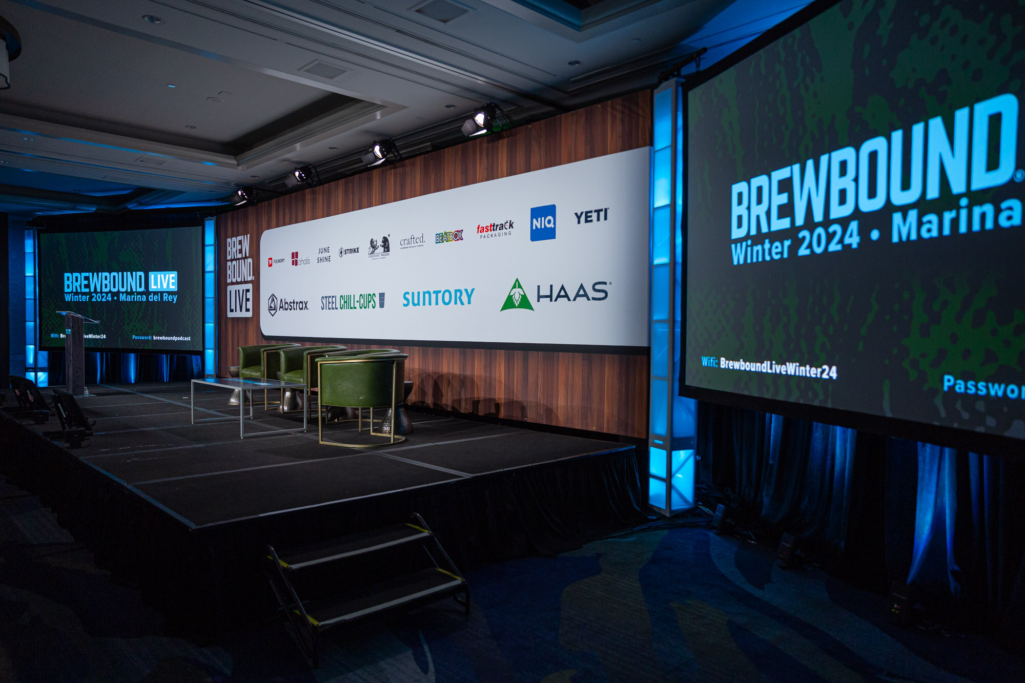 An empty stage with green armchairs and a sponsor wall with a Brewbound Live Winter 2024 screen.