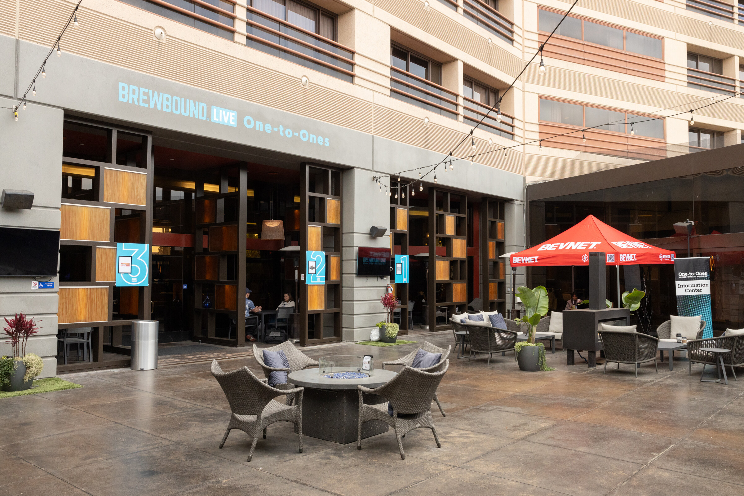A courtyard with chairs, string lights and a Brewbound Live One-to-Ones sign on the building.