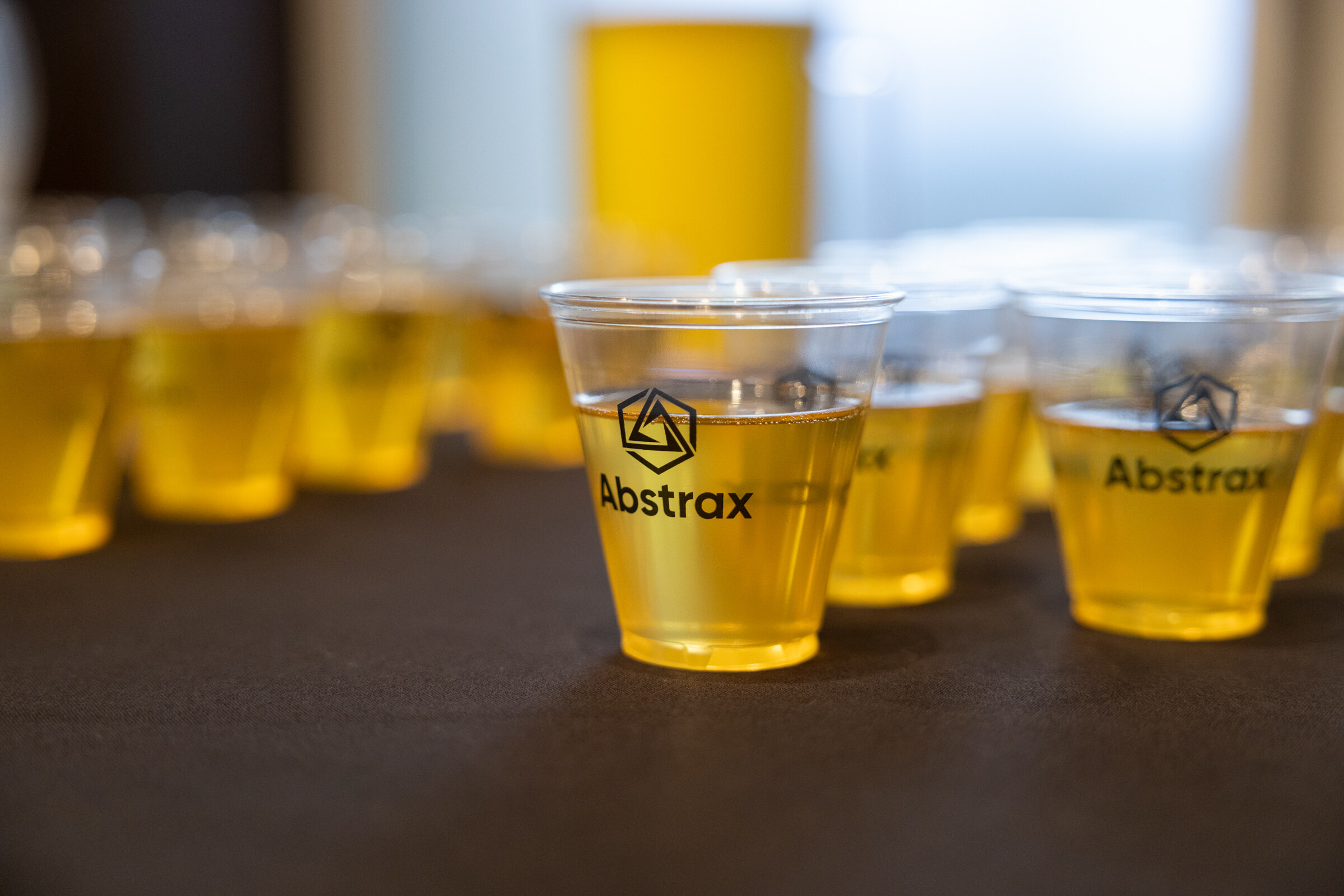 Several clear cups of light beer with Abstrax logos on a table.