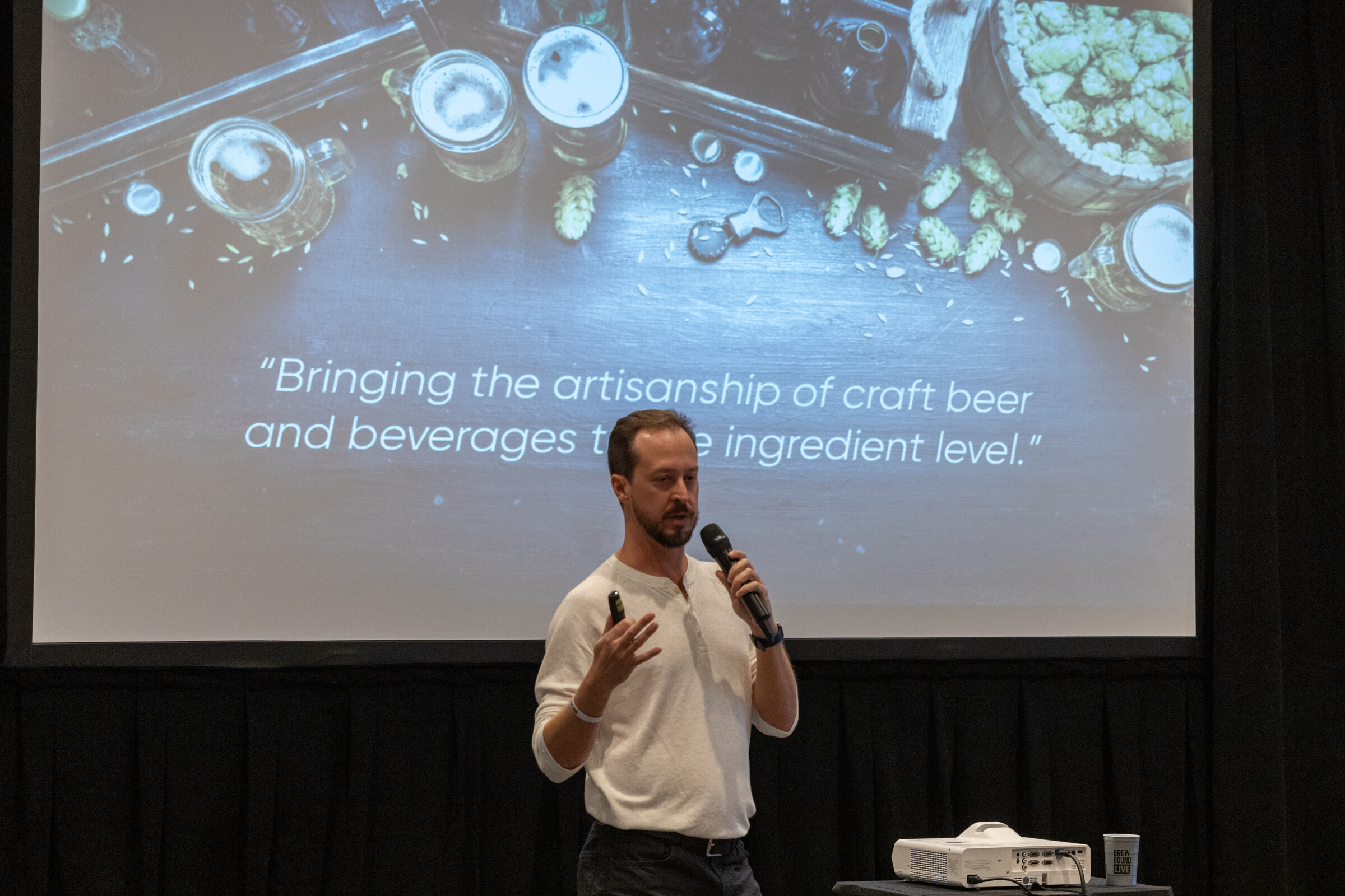 A man stands before a screen with the quote Bringing the artisanship of craft beer and beverages to the ingredient level.