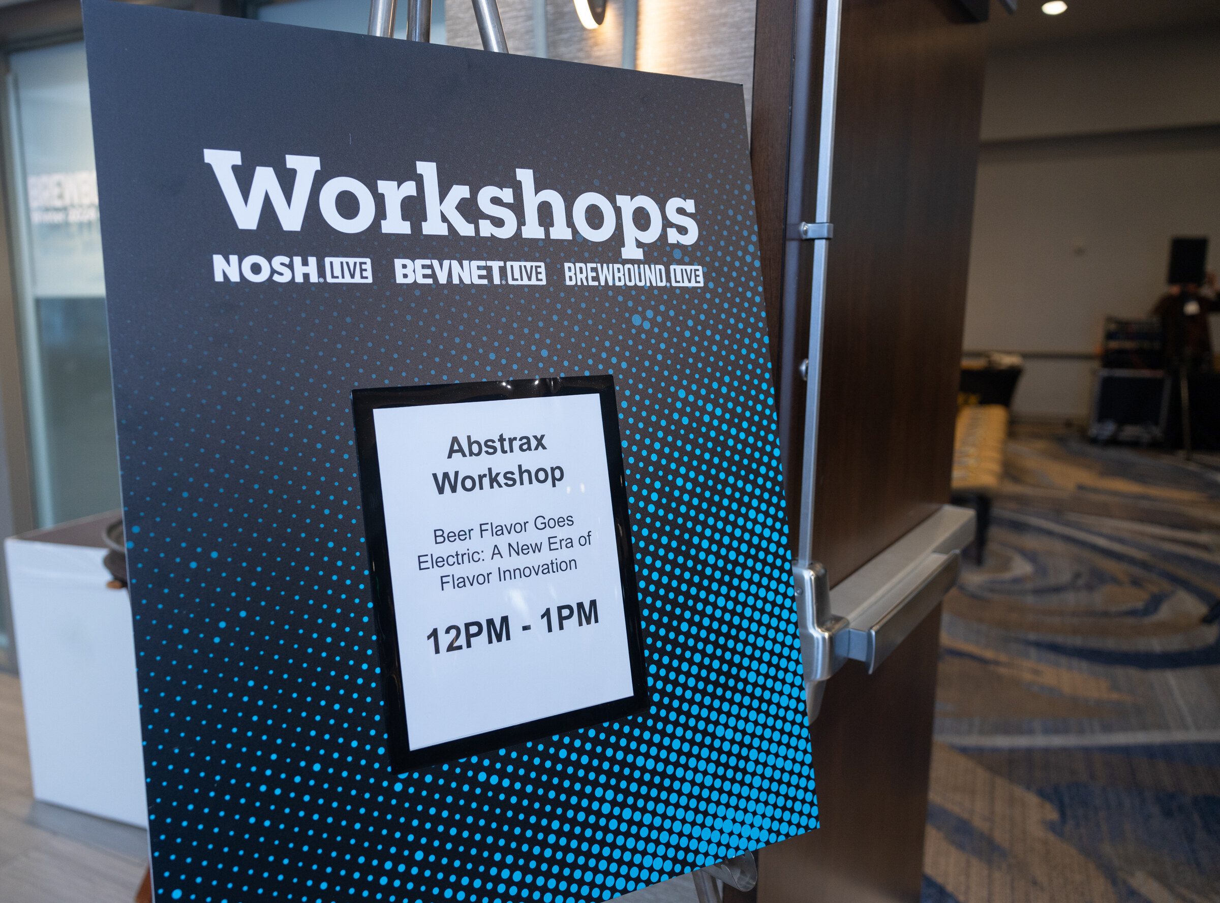 A Workshops sign listing the Abstrax Workshop, Beer Flavor Goes Electric, 12PM to 1PM.