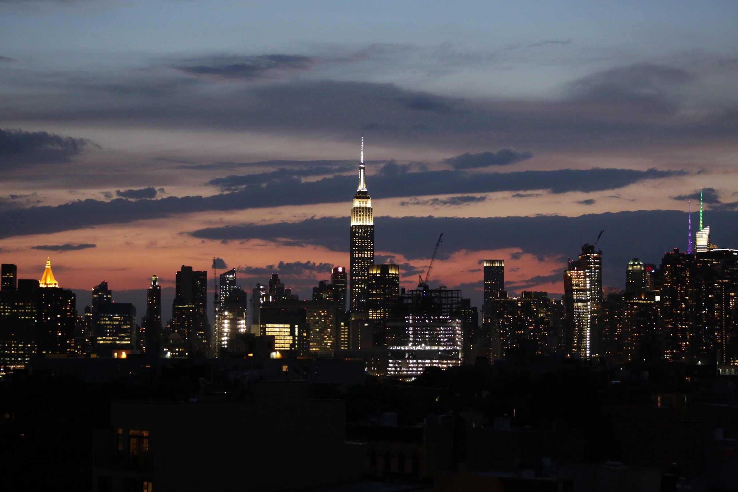 Skyline of Midtown Manhattan at dusk with the lit Empire State Building under clouds.