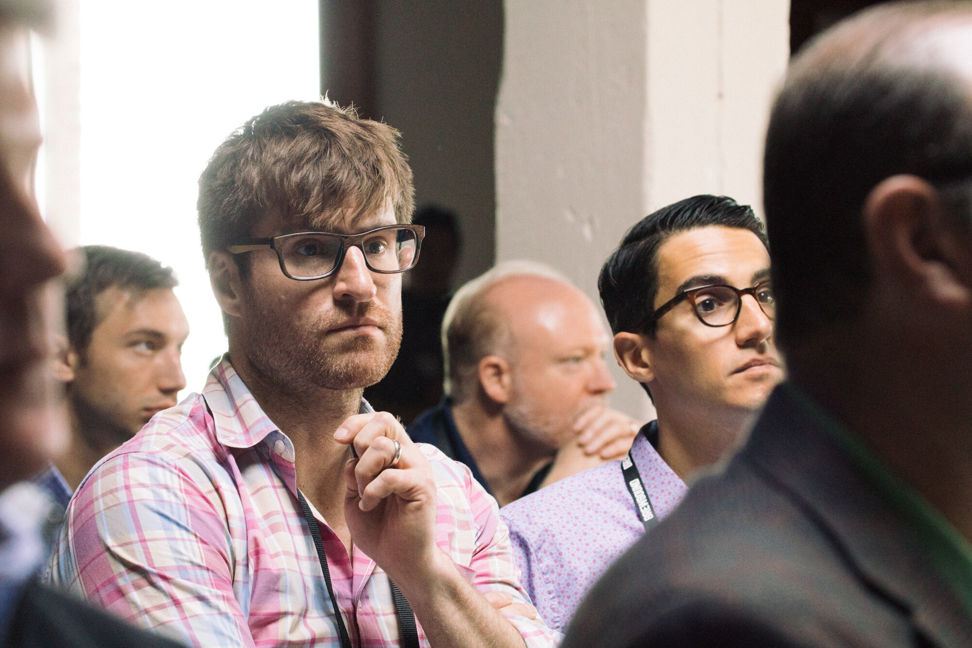 Several seated attendees with lanyards looking toward the stage, two in glasses in the foreground.