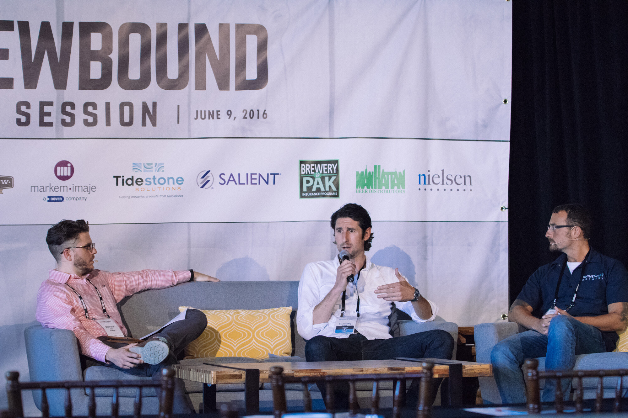 Three men on stage couches, the middle one holding a microphone, in front of a Brewbound Session banner dated June 9, 2016.