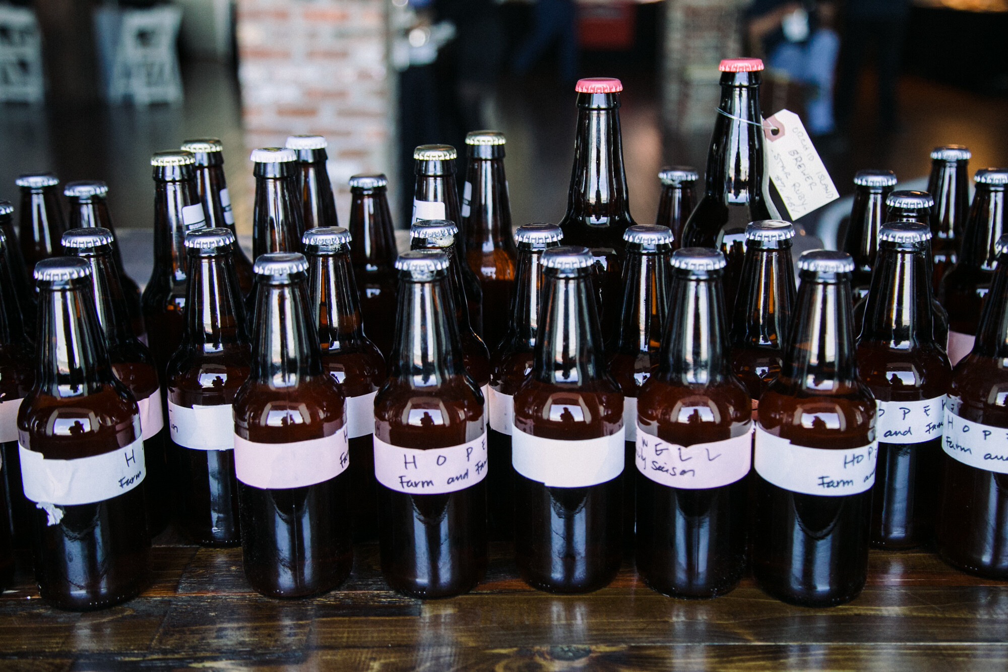 Many dark brown beer bottles with handwritten white labels lined up on a wooden table.