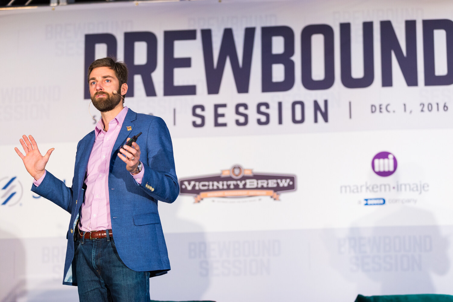 Man in a blue blazer and pink shirt with a clicker in his hand standing in front of a banner reading Brewbound Session, Dec. 1, 2016, with Vicinity Brew and Markem-Imaje logos.