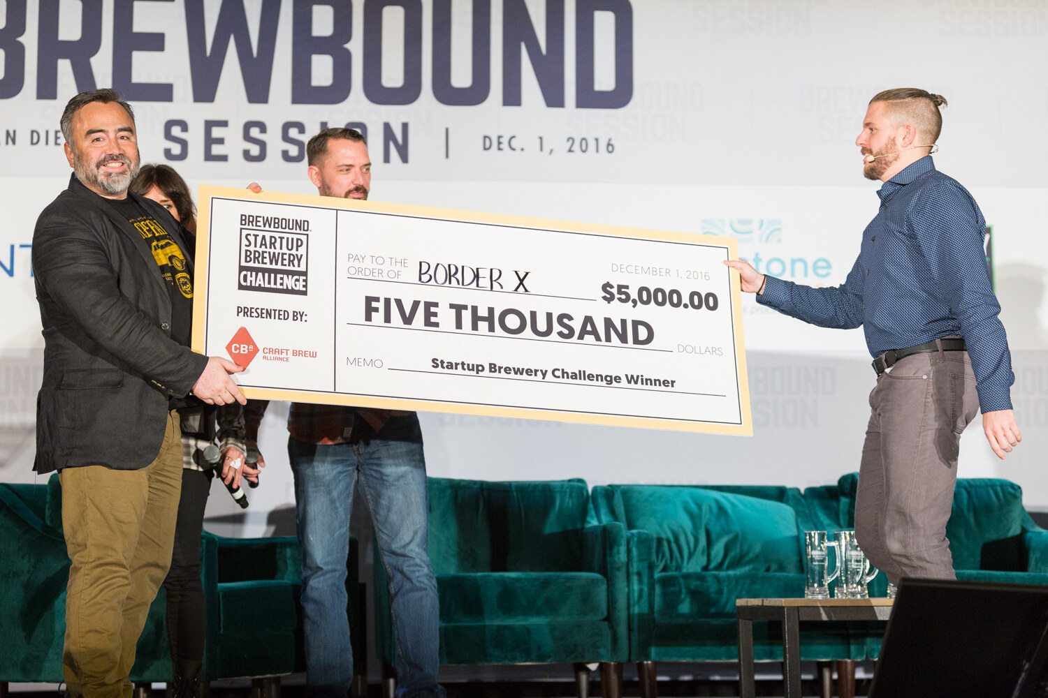 Man in a dark jacket and a man in a navy shirt holding a large check reading Brewbound Startup Brewery Challenge, Border X, Five Thousand, $5,000.00, presented by Craft Brew Alliance, dated December 1, 2016.