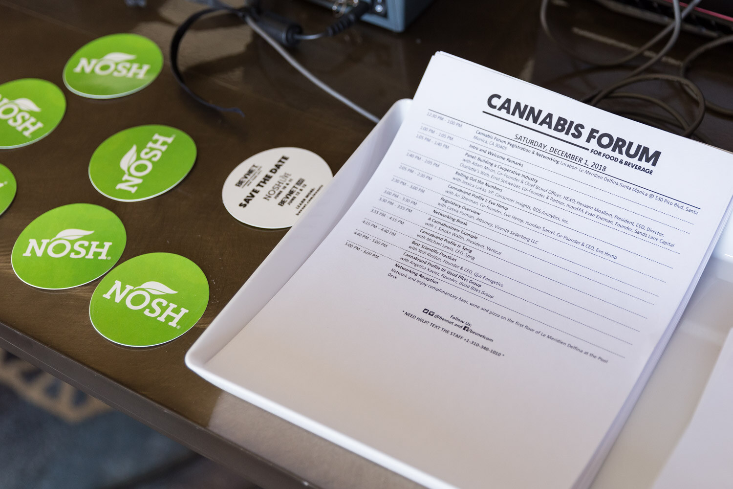 A white tray holding a Cannabis Forum agenda sheet and round green NOSH stickers.