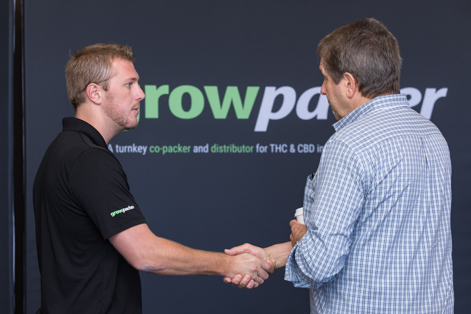 Two men shaking hands in front of a black growpacker banner.