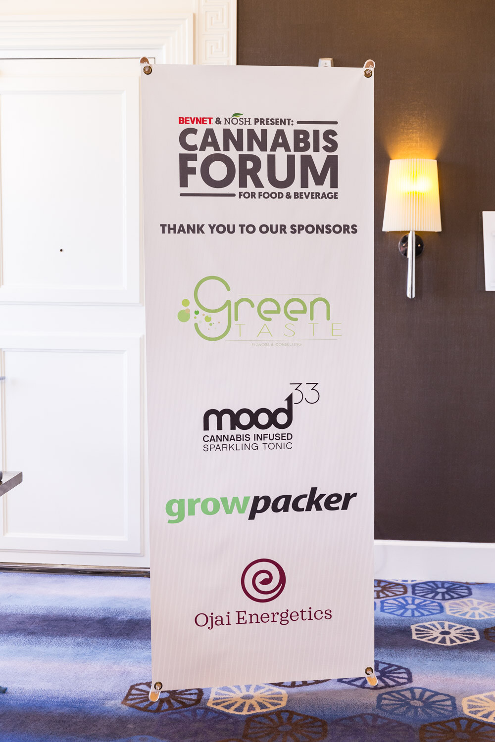 A tall white banner reading Cannabis Forum for Food and Beverage with four sponsor logos stacked beneath it.