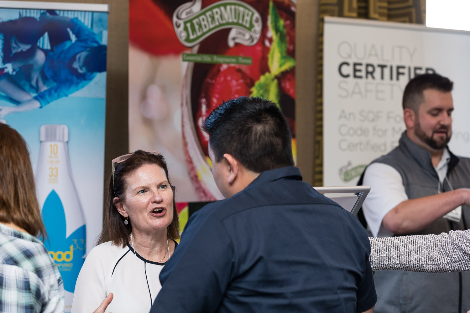 A woman speaking with two men in front of banners for mood bottles and Lebermuth.