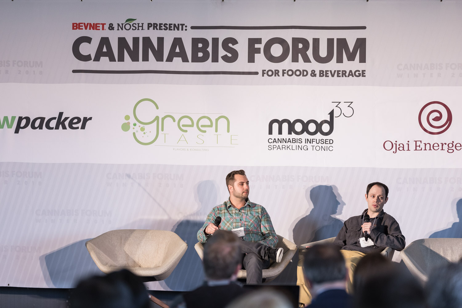 Two seated men on a stage beneath a Cannabis Forum for Food and Beverage banner, with audience heads in the foreground.