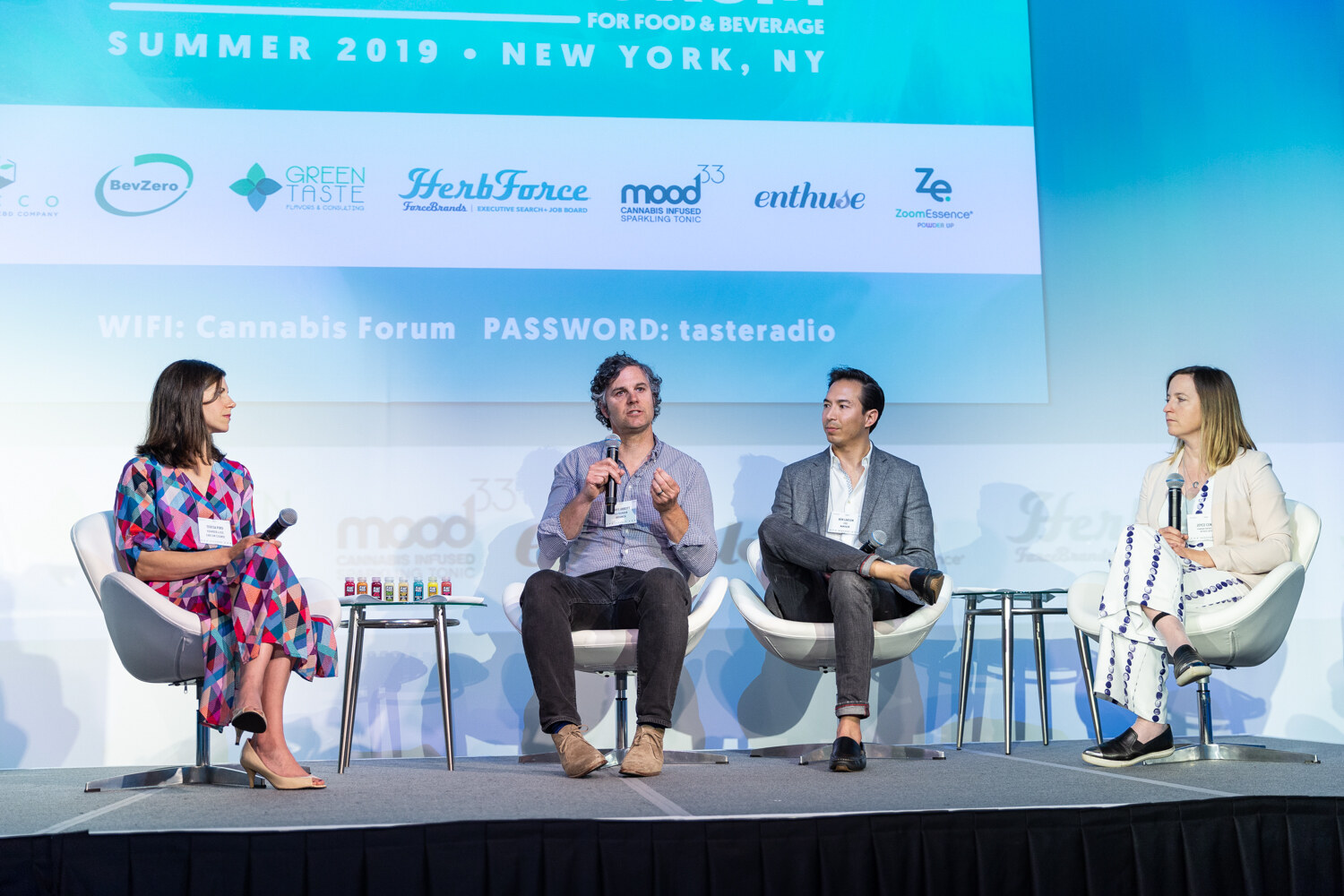 Four people sit in white lounge chairs on a stage with side tables, below a banner of sponsor logos including Green Taste, HerbForce, Mood33 and Enthuse.