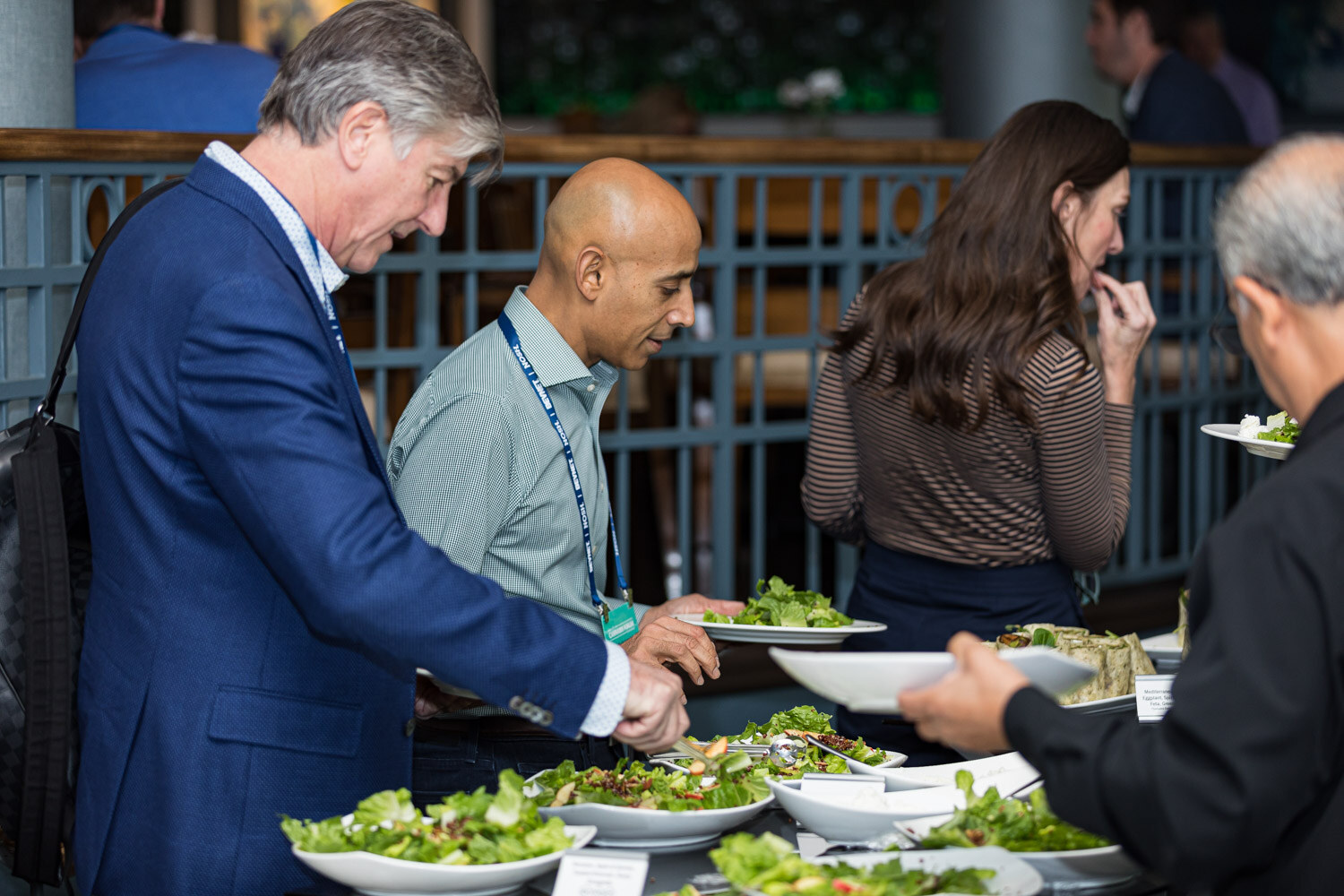Several people in conference lanyards serve themselves salads from bowls at a buffet table.