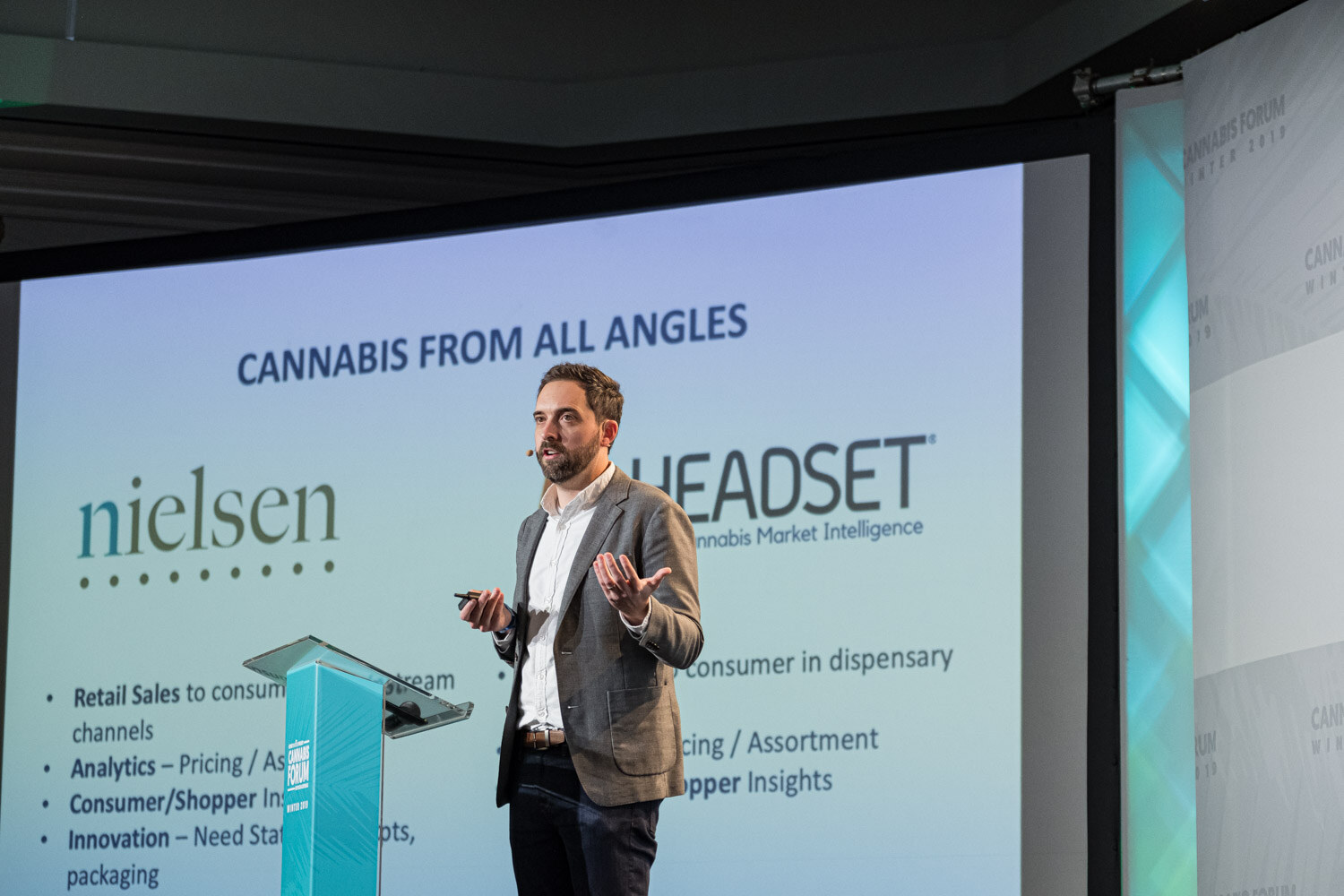 A bearded man in a gray blazer stands at a podium in front of a large slide titled Cannabis From All Angles showing the Nielsen and Headset logos.