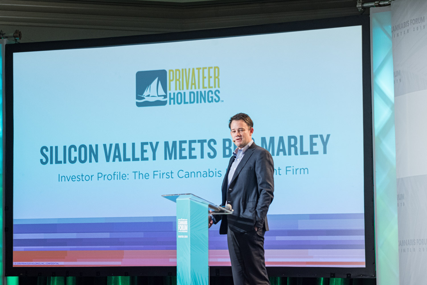 A man in a dark suit stands at a podium in front of a slide with the Privateer Holdings logo and the title Silicon Valley Meets Bob Marley, Investor Profile: The First Cannabis Investment Firm.