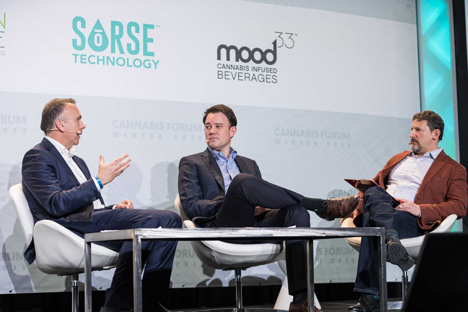 Three men sit in white lounge chairs around a low table, one gesturing as he speaks and one in a rust-colored jacket holding notes, with Sorse Technology and Mood33 logos behind them.