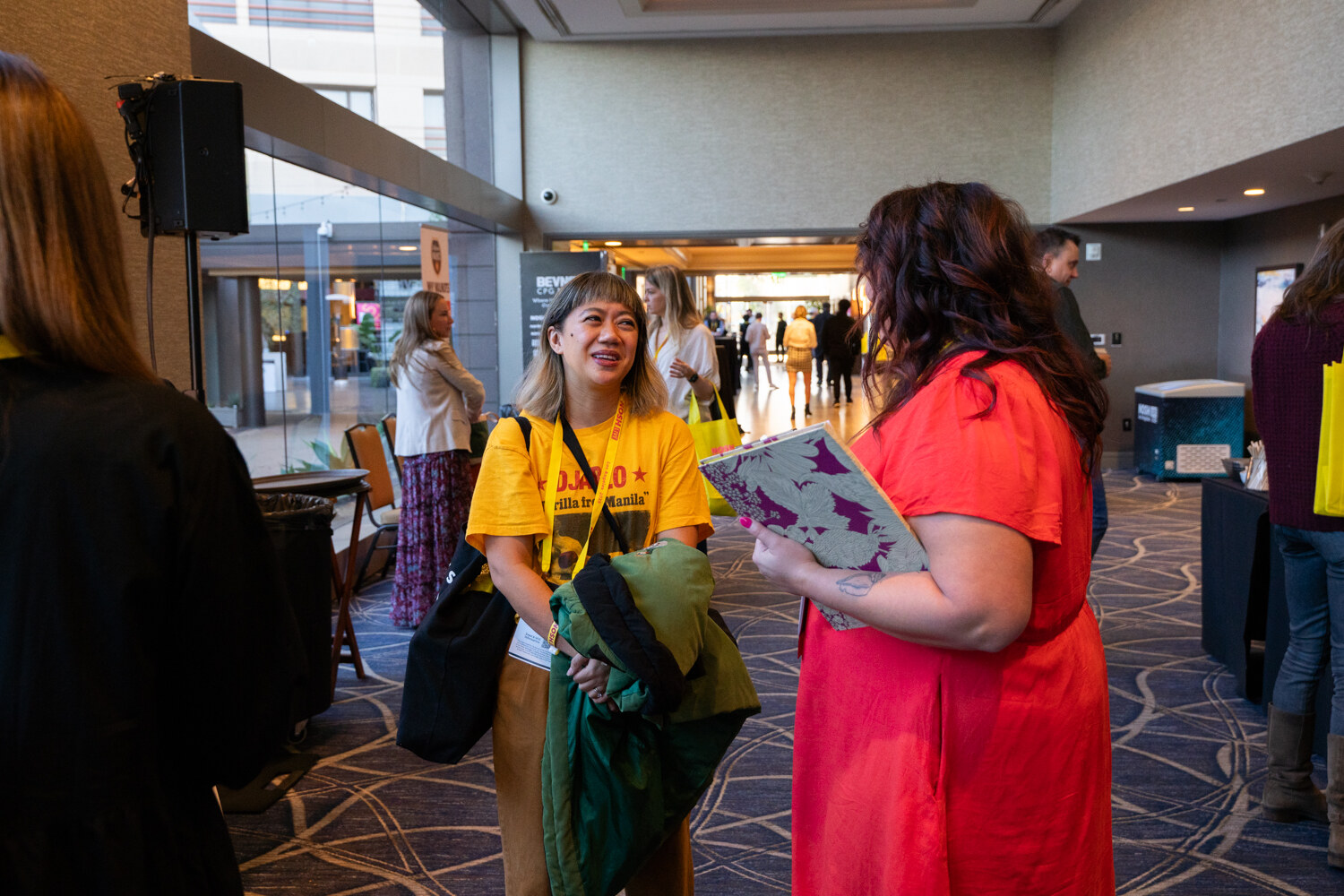 A woman in a yellow t-shirt and a woman in a red dress talking in a hotel lobby.