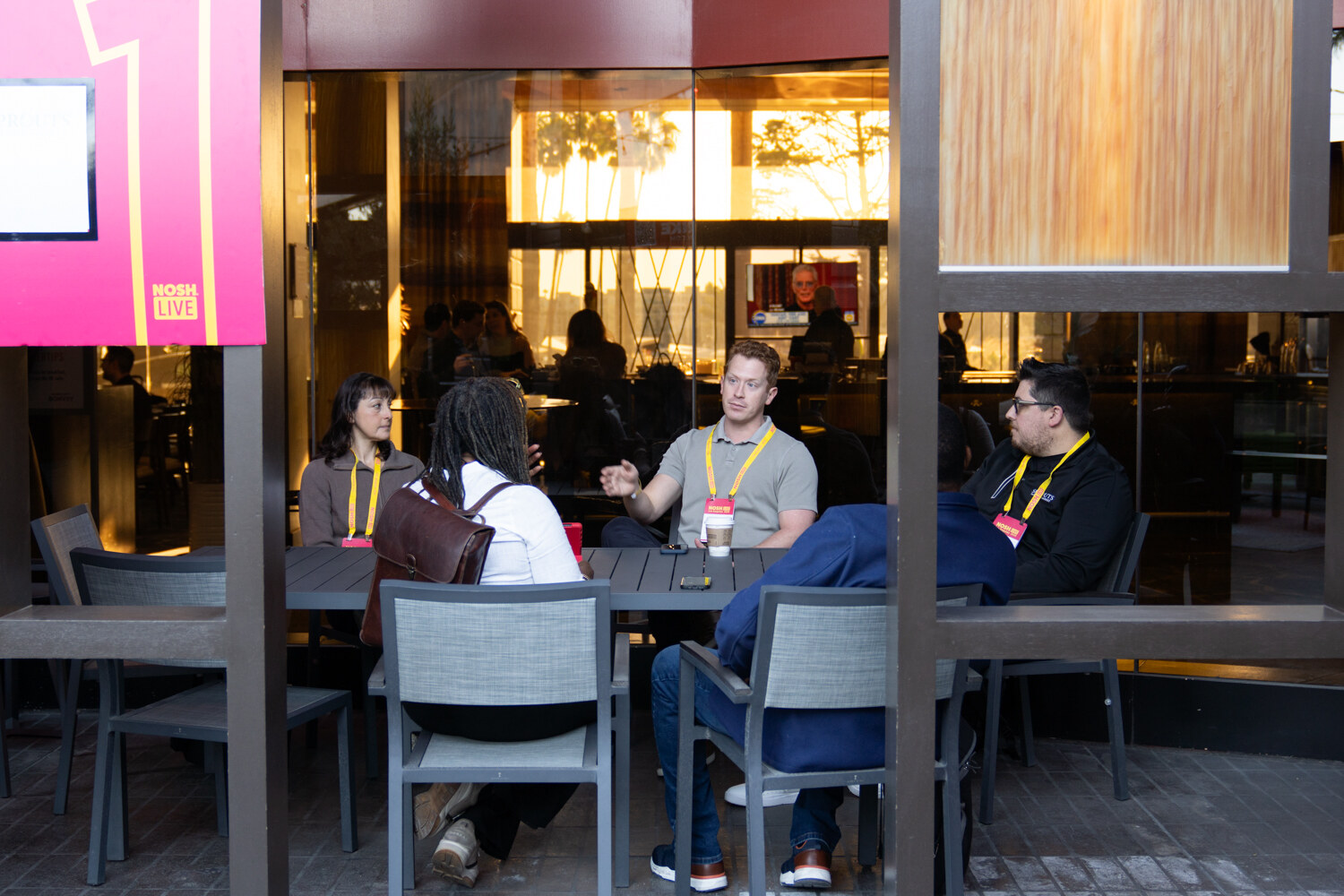 Four people seated at an outdoor table seen through a partition marked with a pink number.