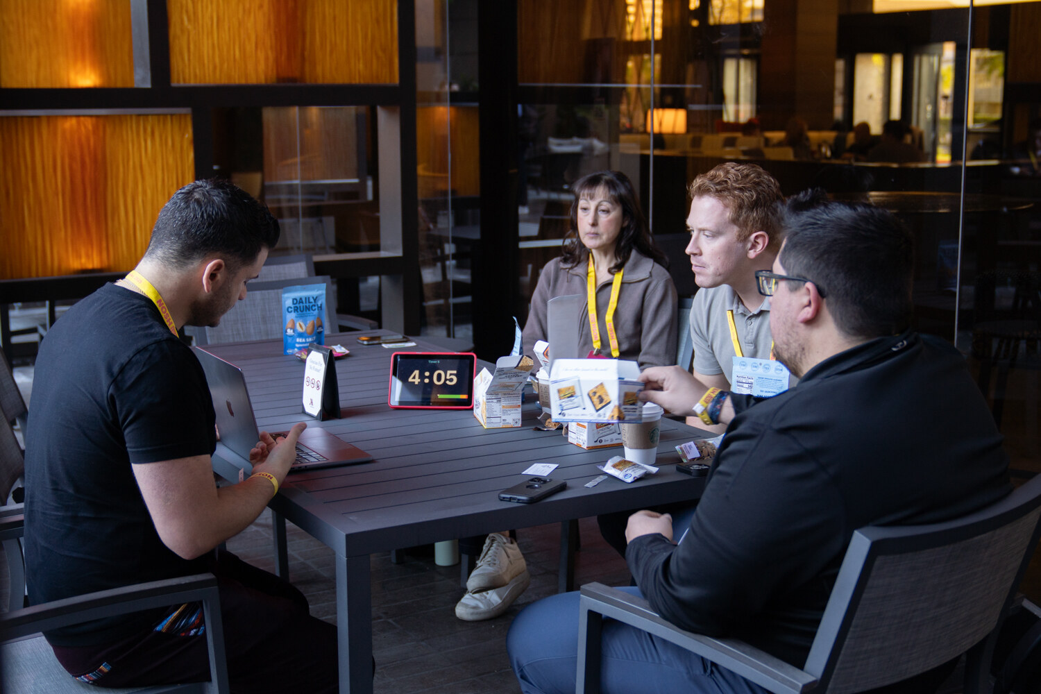 Four people at a small table with coffee cups and a red countdown timer showing 4:05.