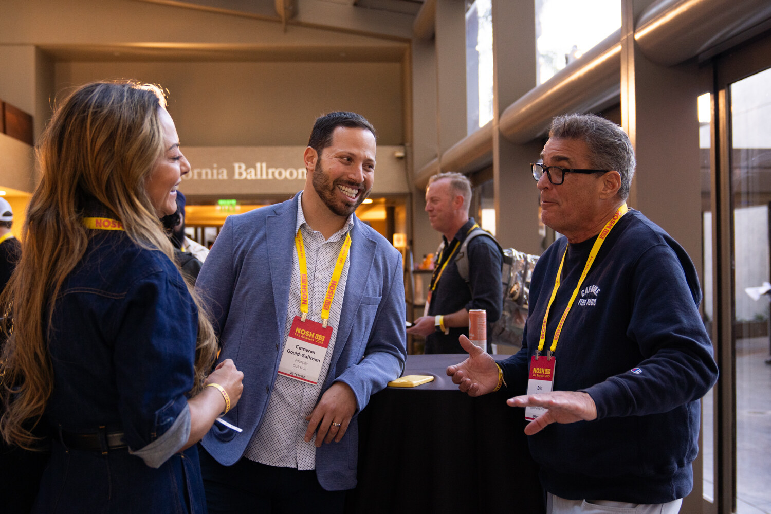Three people with lanyards in conversation next to a sign reading California Ballroom.