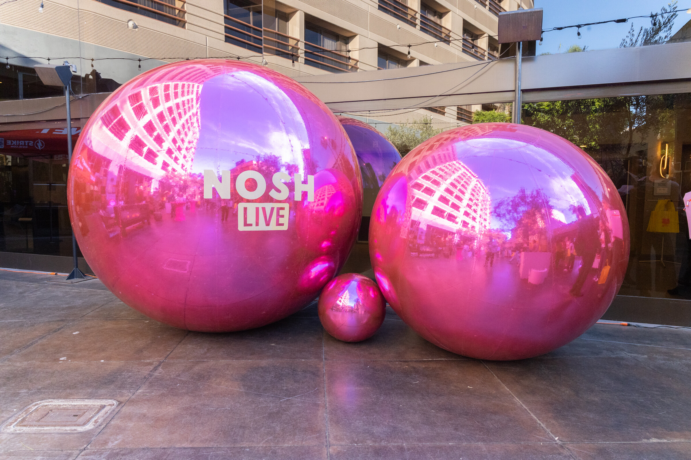 Large reflective pink spheres with a Nosh Live logo on the courtyard stage.