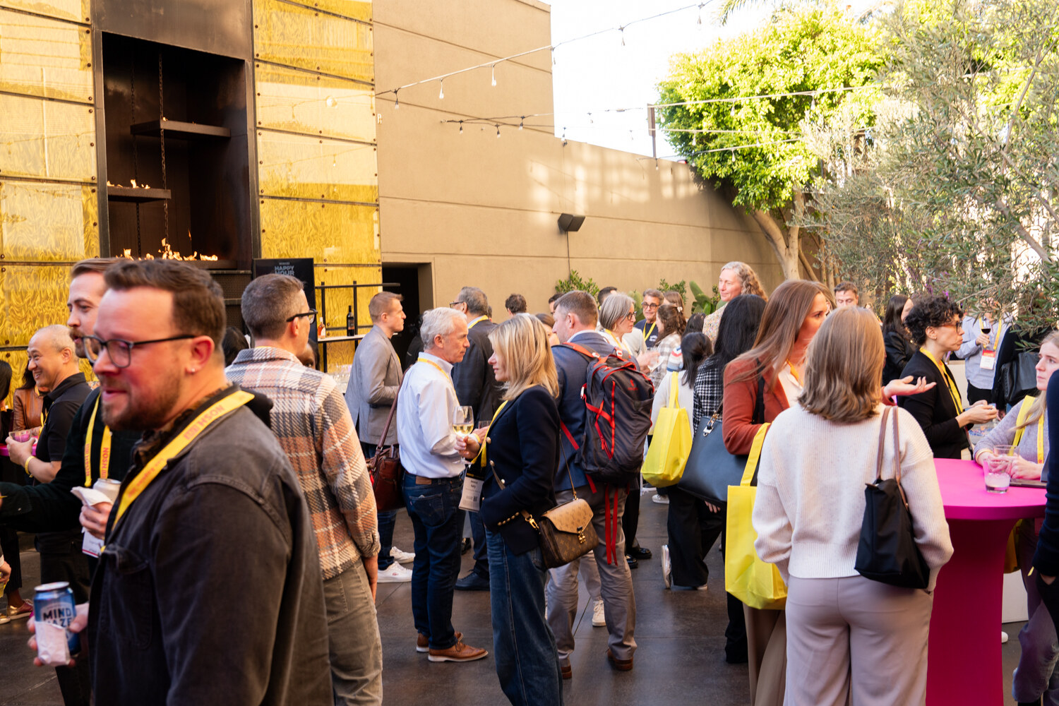 A crowd of attendees in lanyards and yellow tote bags talking in an outdoor courtyard.
