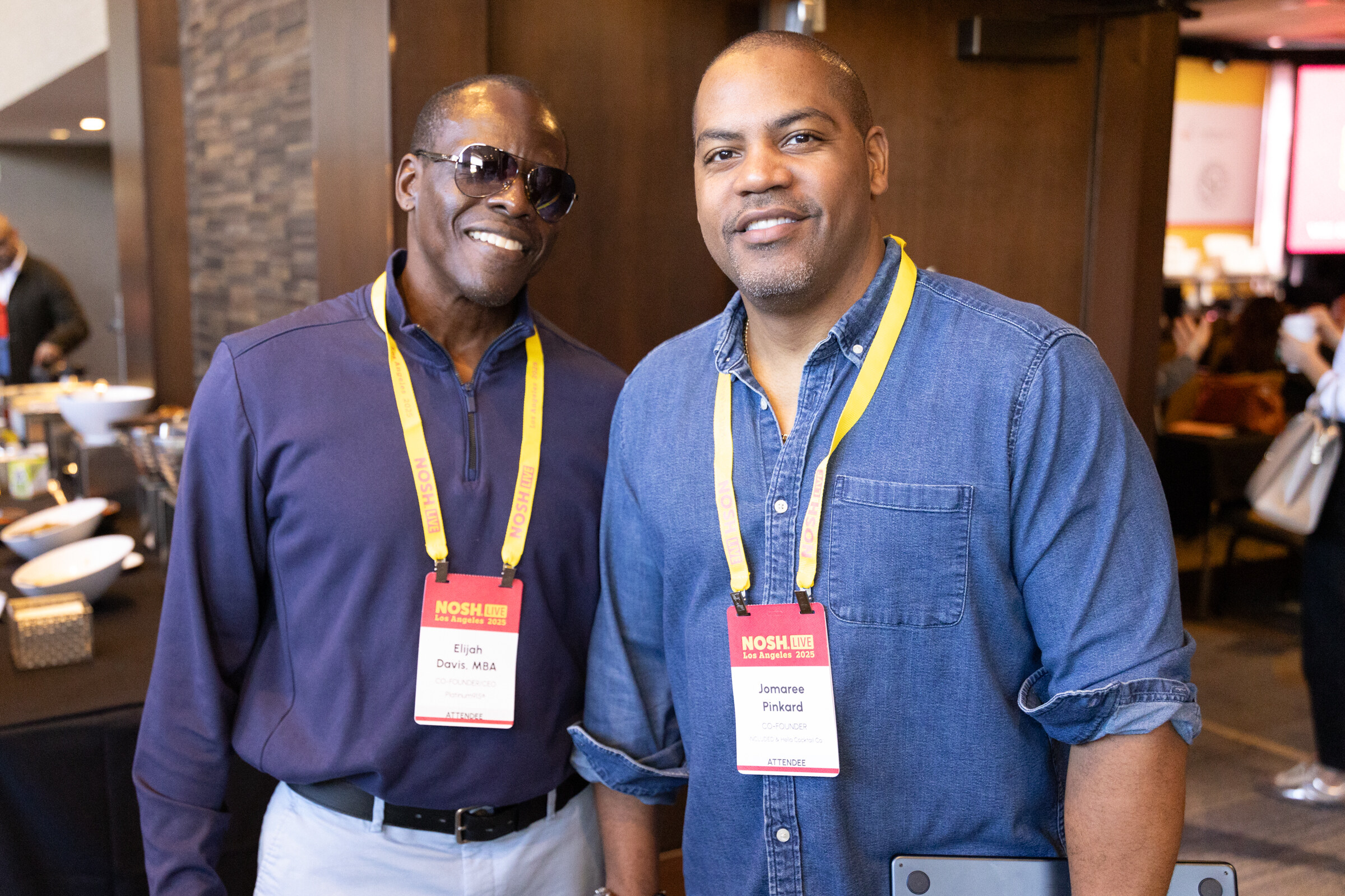 Two men wearing Nosh Live lanyards and badges smiling at the camera.
