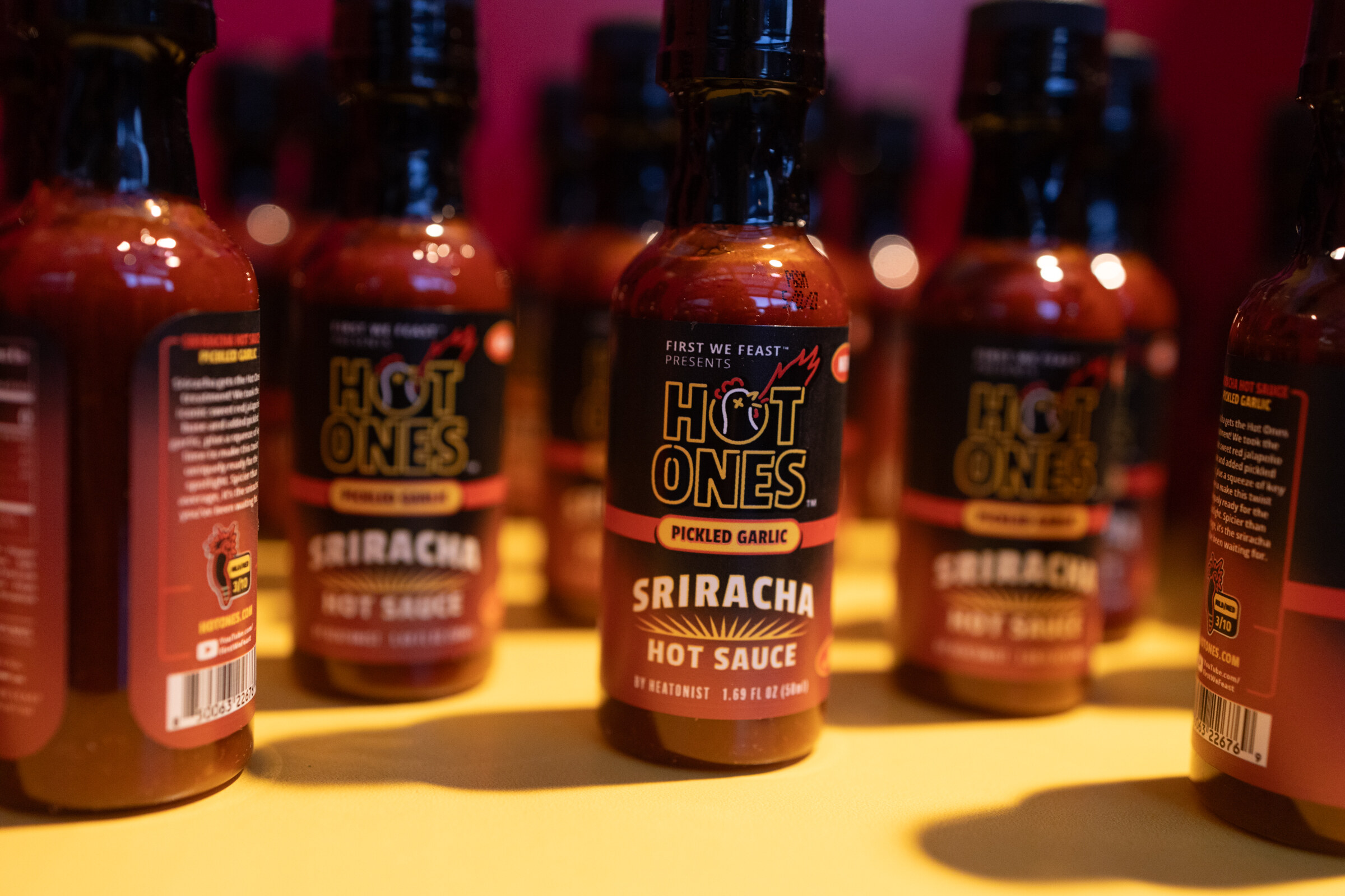 Rows of Hot Ones Pickled Garlic Sriracha hot sauce bottles on a yellow shelf.