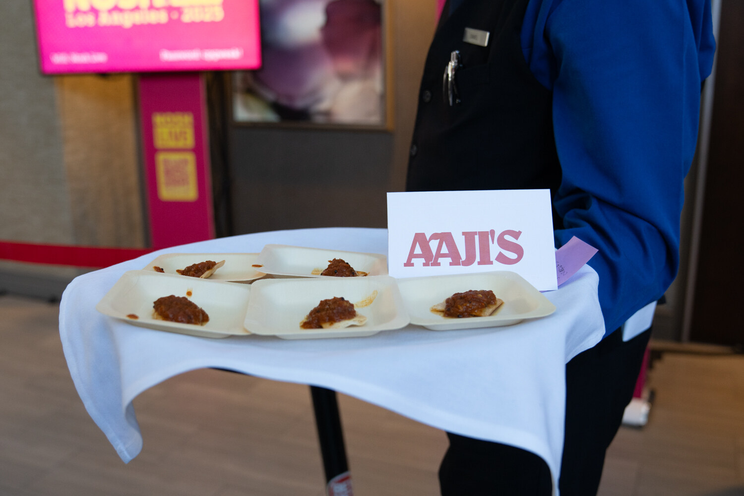 A tray with small servings of a spiced chutney-style dish and a tent card reading Aaji's.