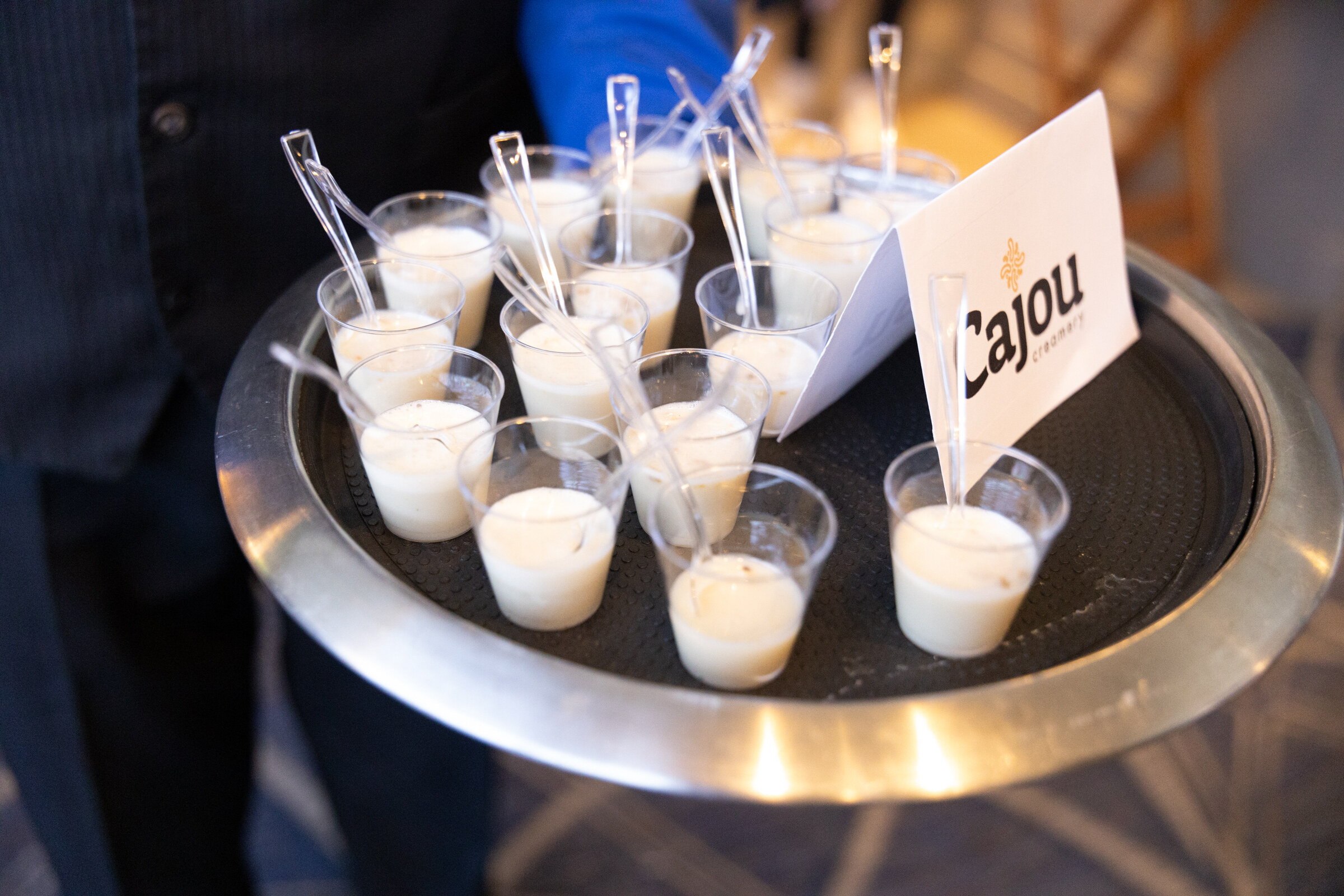 A round tray of small white sample cups with spoons and a card reading Cajou.
