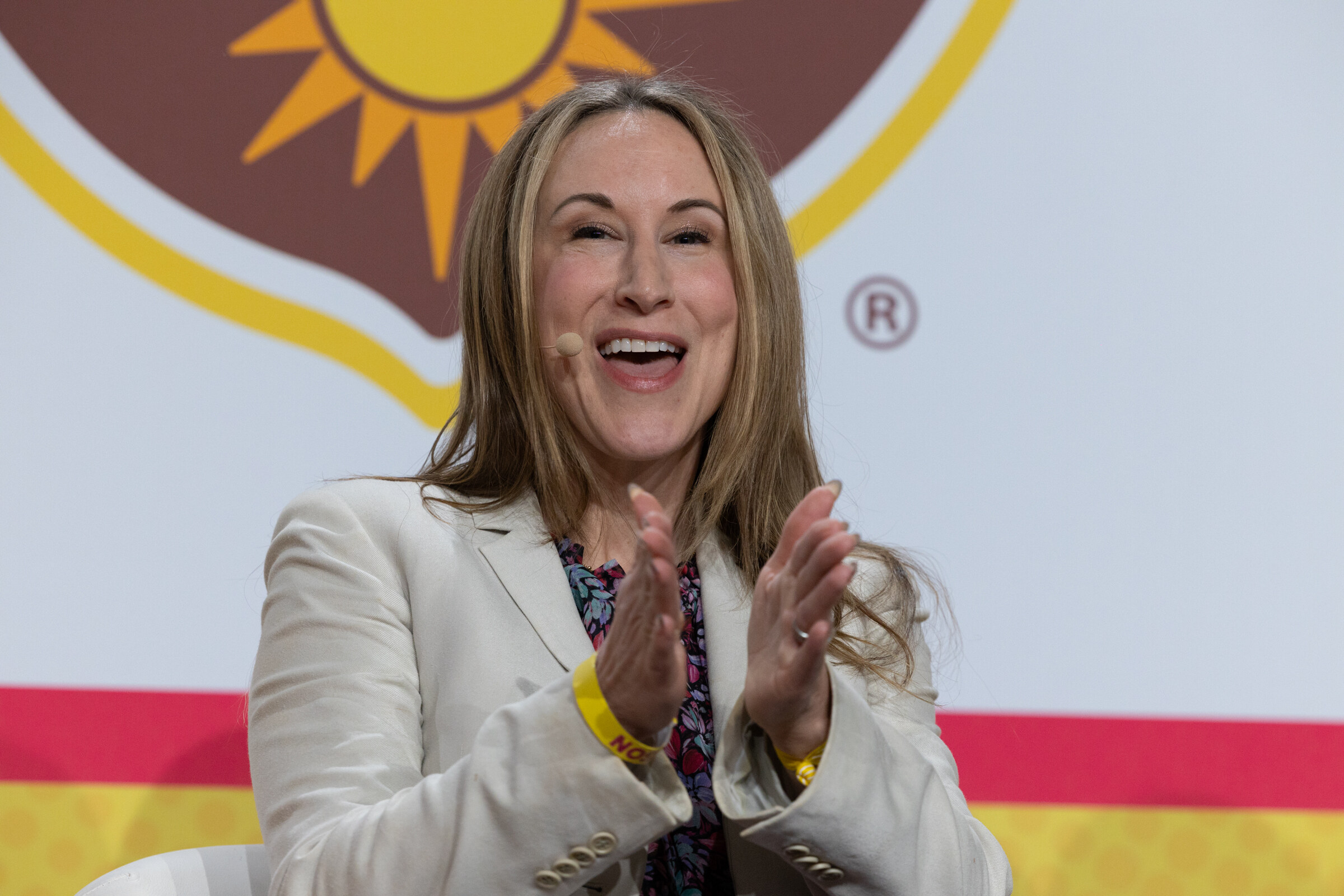 A smiling woman in a cream blazer clapping in front of a California Walnuts backdrop.