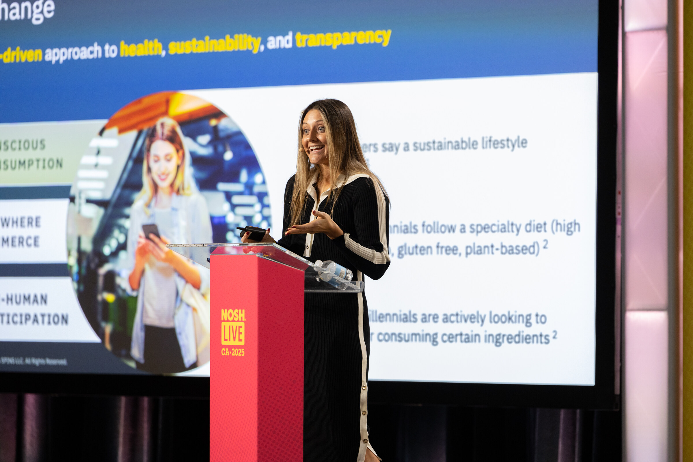 A woman at a podium beside a projected slide about conscious consumption and a values-driven approach to health.