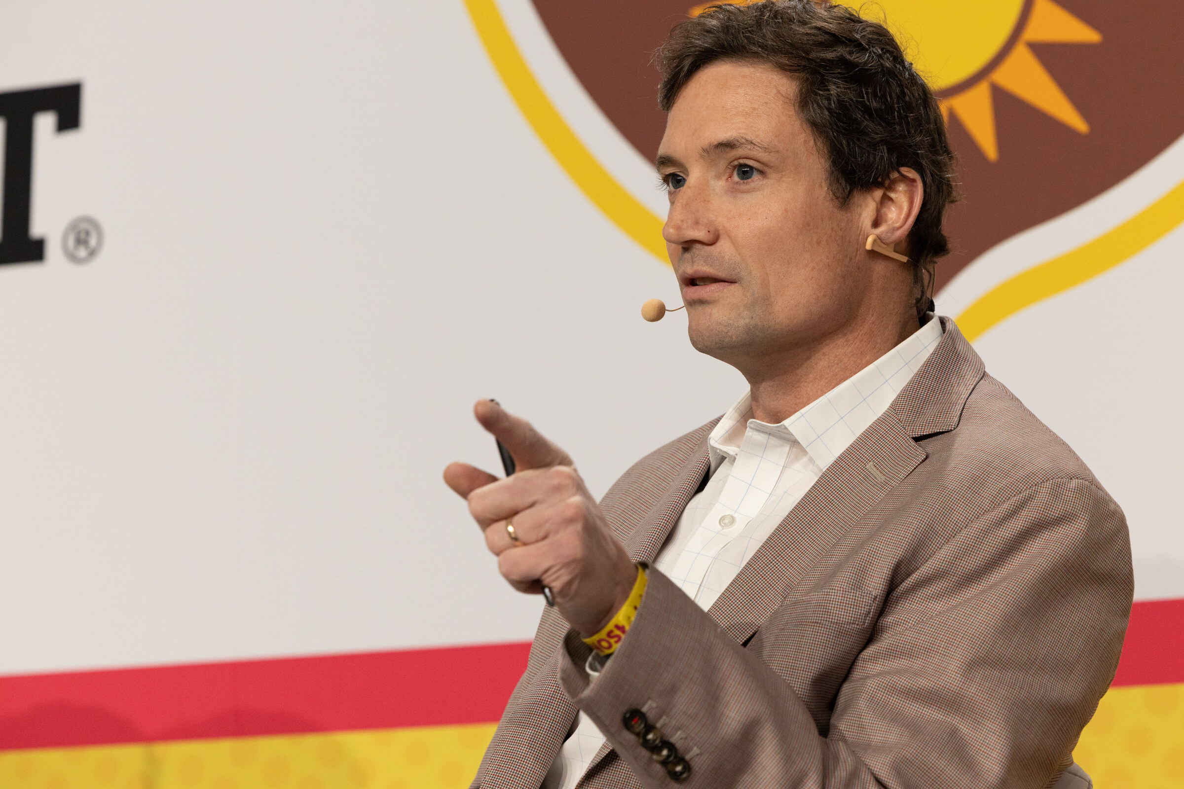 A man in a tan blazer pointing as he speaks in front of a California Walnuts logo.