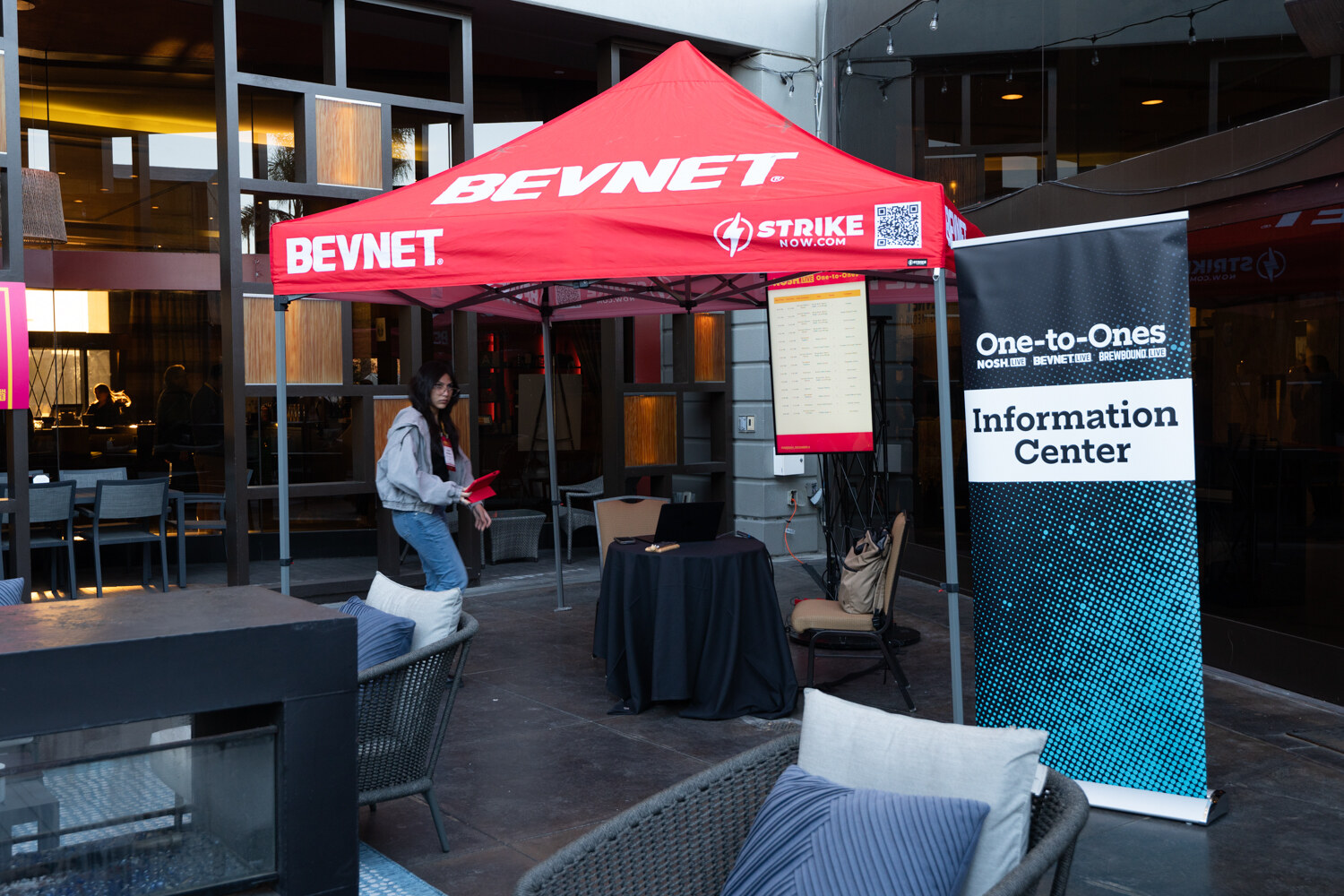 A red BevNET tent with a One-to-Ones Information Center banner on an outdoor patio.