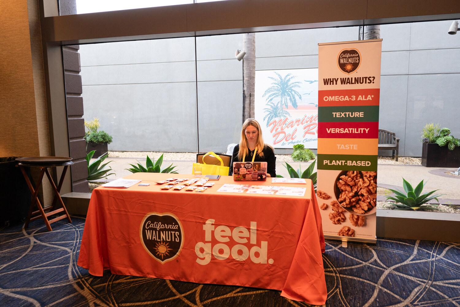 A woman at a table with an orange cloth reading feel good and a California Walnuts Why Walnuts banner.