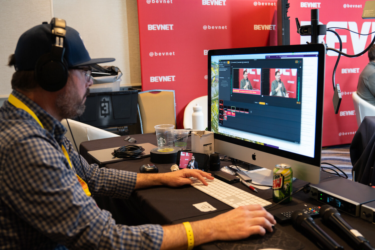 A man in headphones and a blue cap working at a computer showing streaming software in front of a BevNET backdrop.